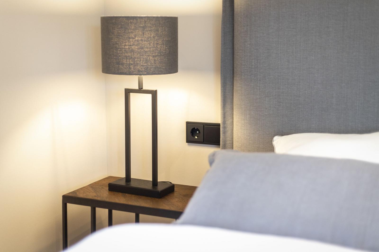 Bedroom with nightstand, lamp, and gray headboard.