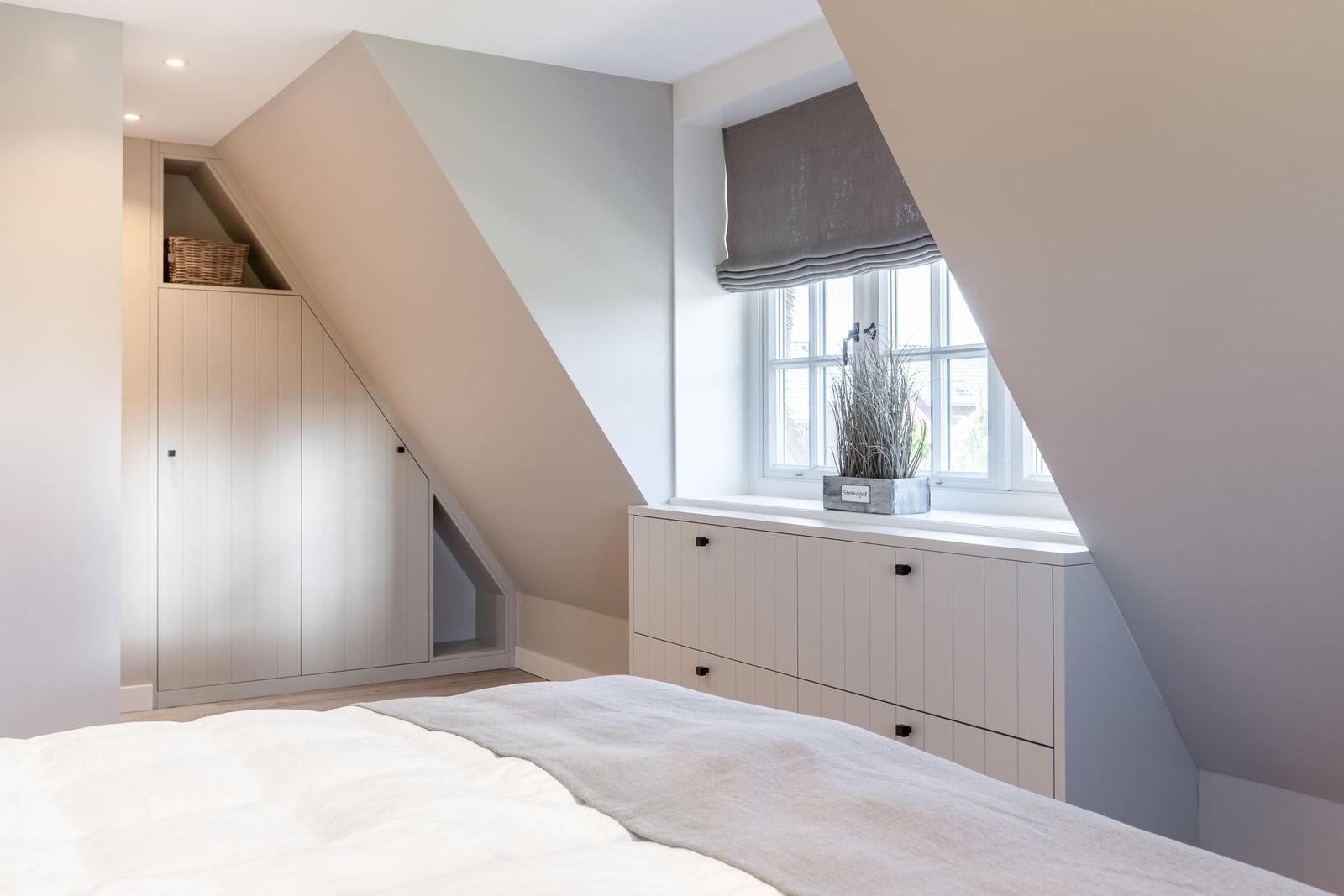 Bedroom with sloped ceiling, window, and white cabinets.