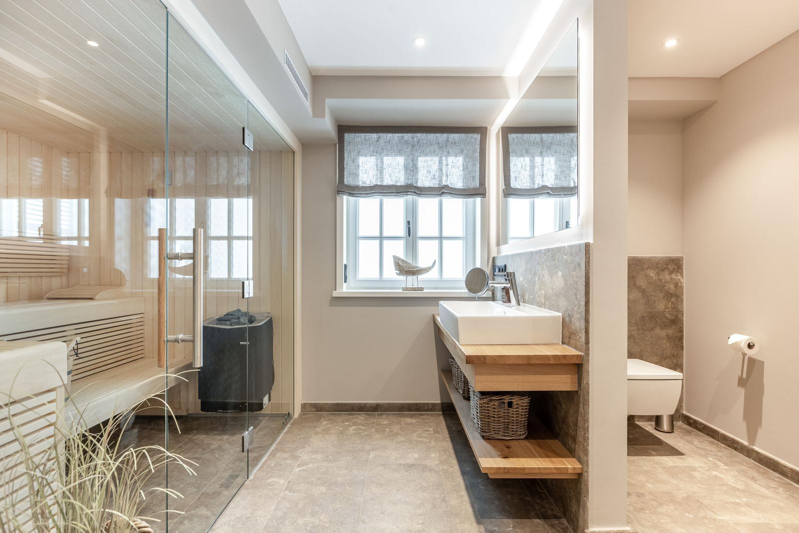 Bathroom with shower, sink, and toilet. Wooden vanity and glass partition.