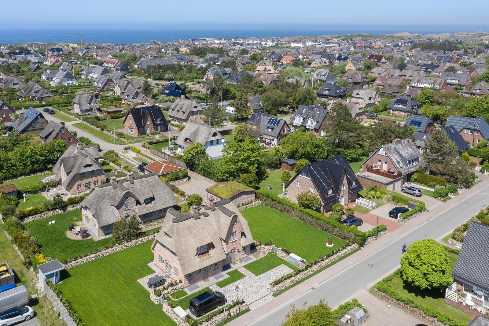 Aerial view of a coastal town with thatched-roof houses and green lawns near the sea.