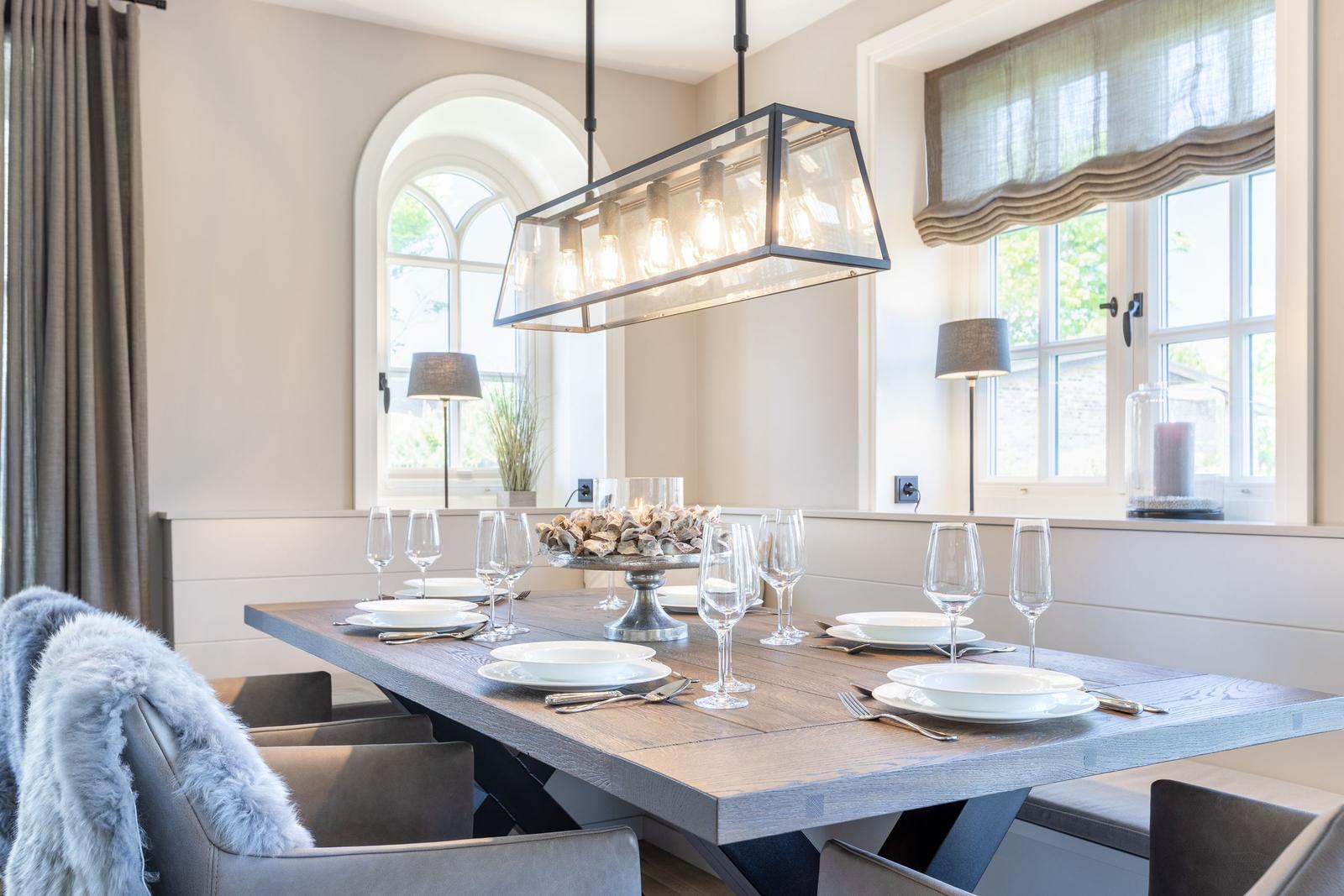 Dining room with long wooden table, chairs, and windows with curtains.