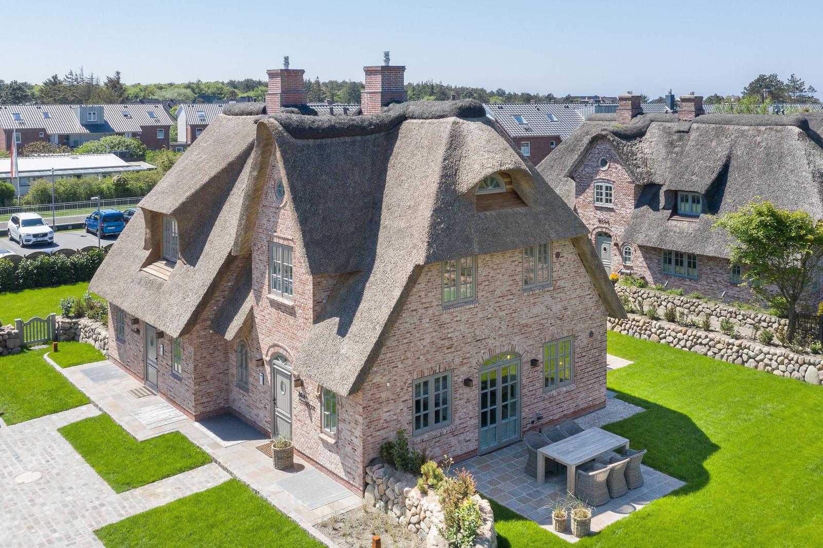 House with thatched roof, garden, and terrace with table and chairs.