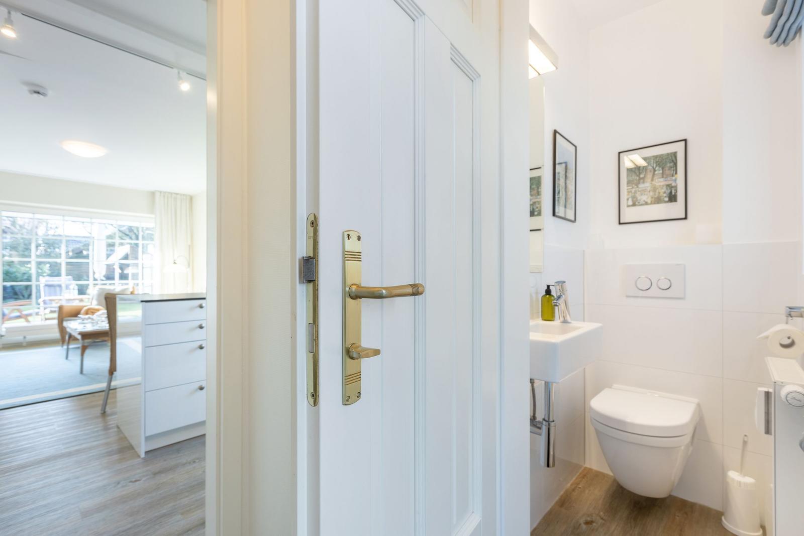 Hinter einer weißen Tür ist ein Badezimmer mit Toilette und Waschbecken sichtbar.