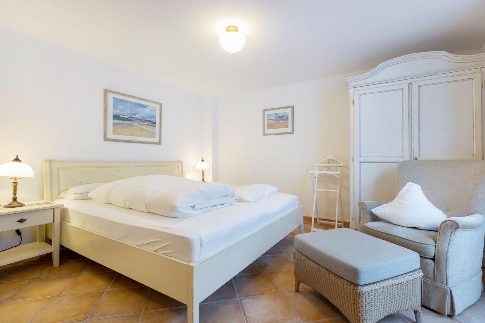 Schlafzimmer mit Bett, Schrank und Sessel. Wandbilder und Steintile.