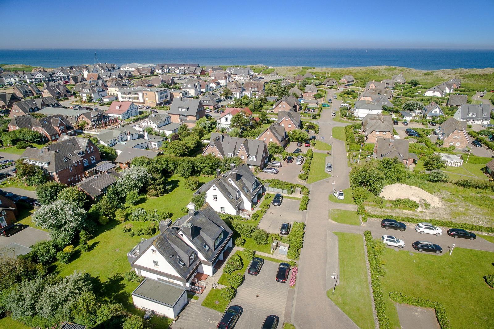 Aerial view of houses with gardens and the sea in the background.