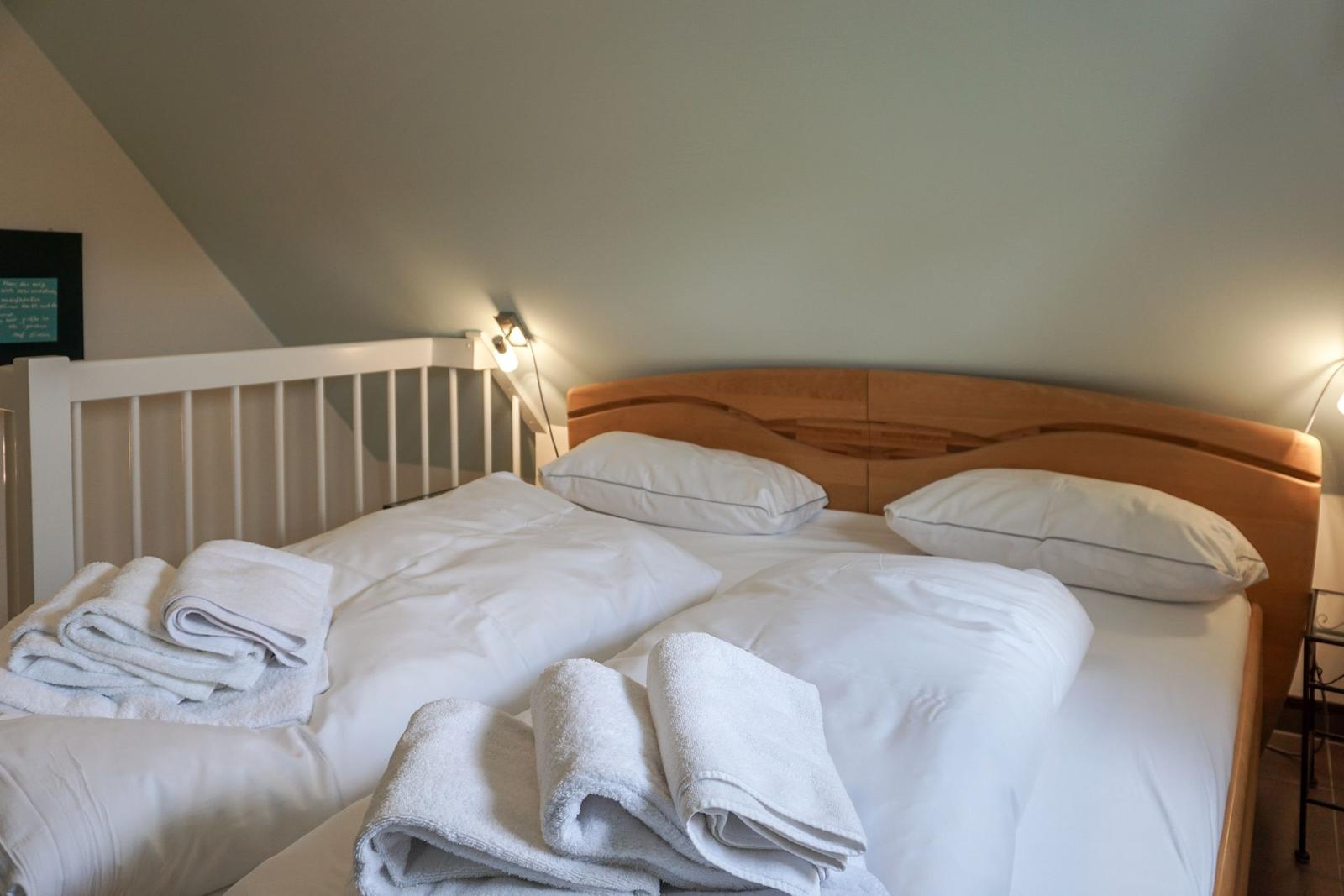 Double bed with white linens and folded towels under a sloped ceiling.