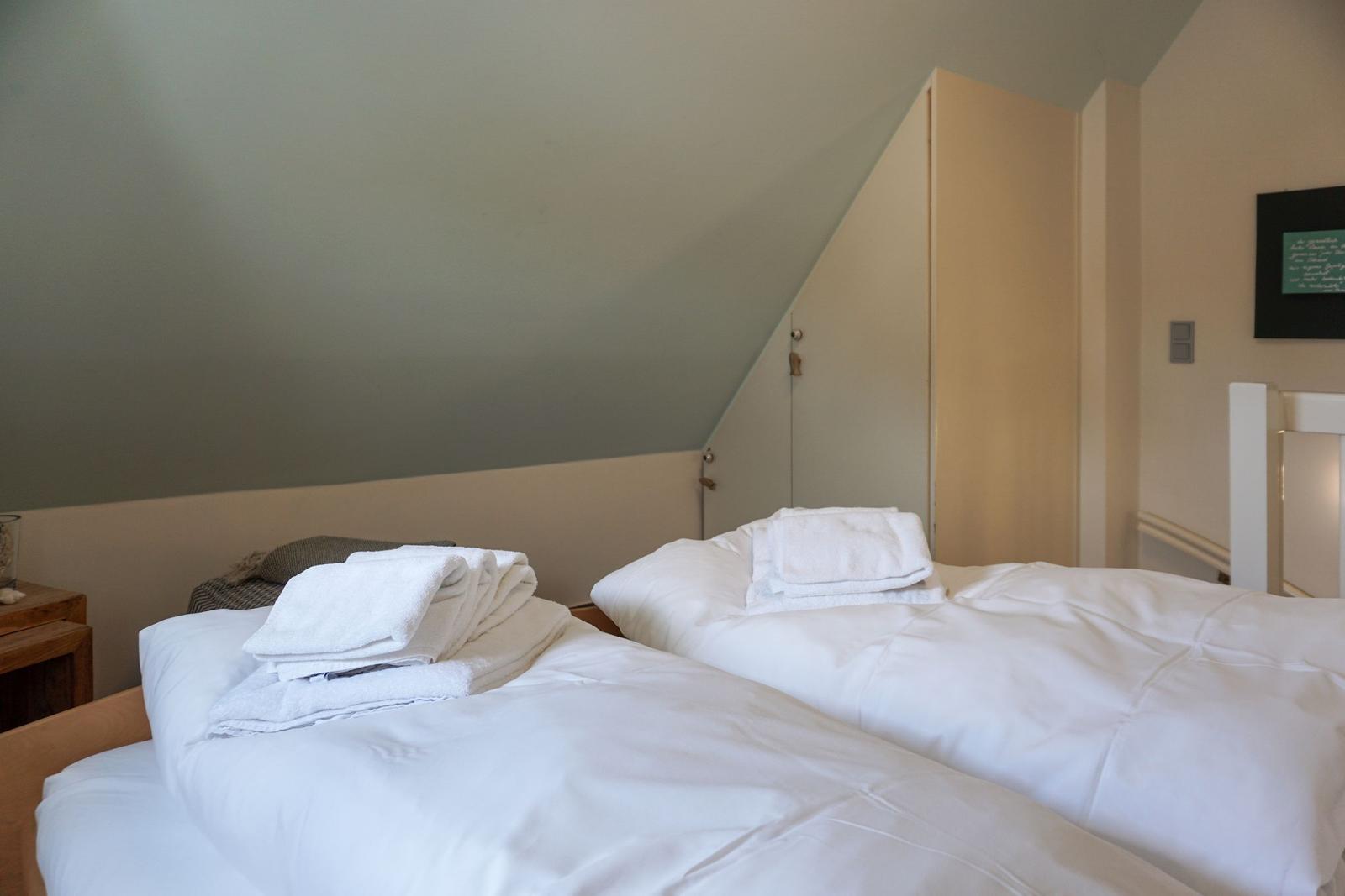 Two beds with white bedding and folded towels under sloped ceiling walls.