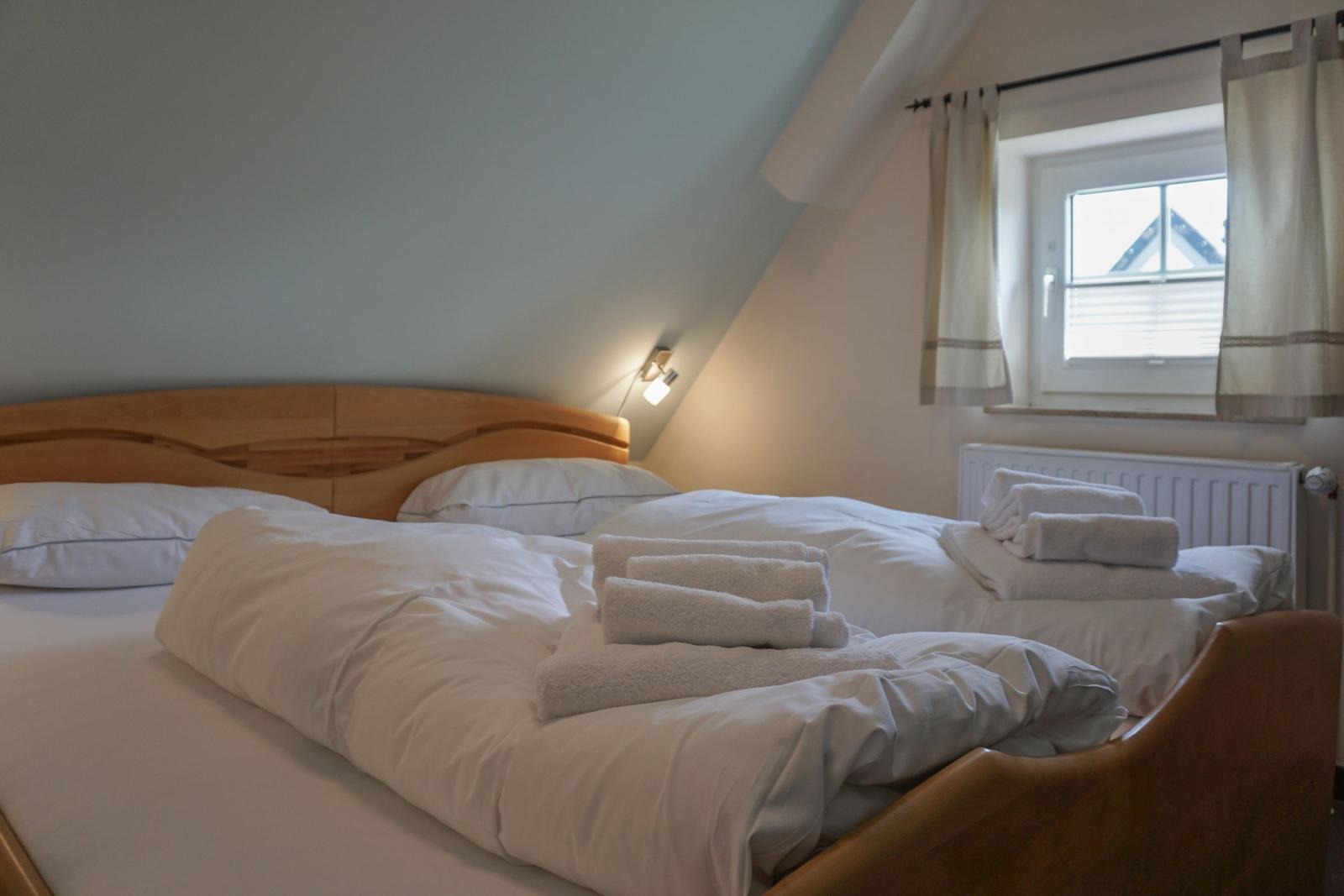 Double bed with white bedding and folded towels under sloped ceiling.