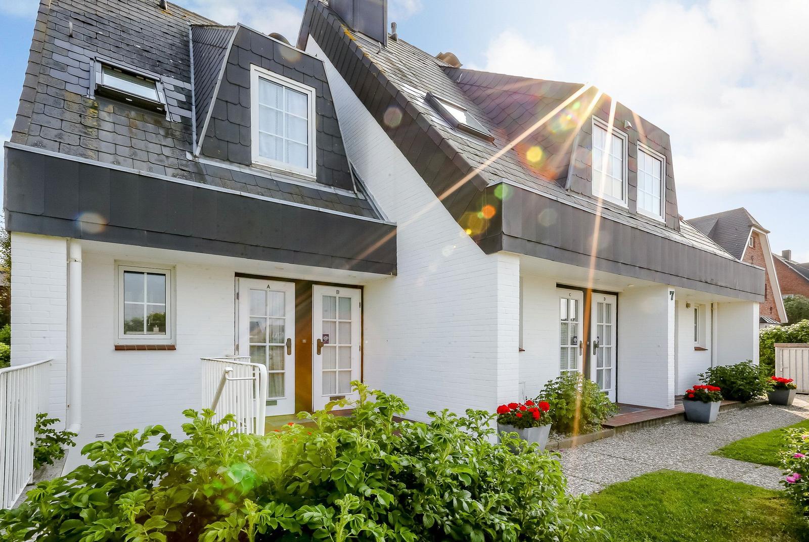 White villa with dark roof and multiple entrances. Garden with flowers and grass.