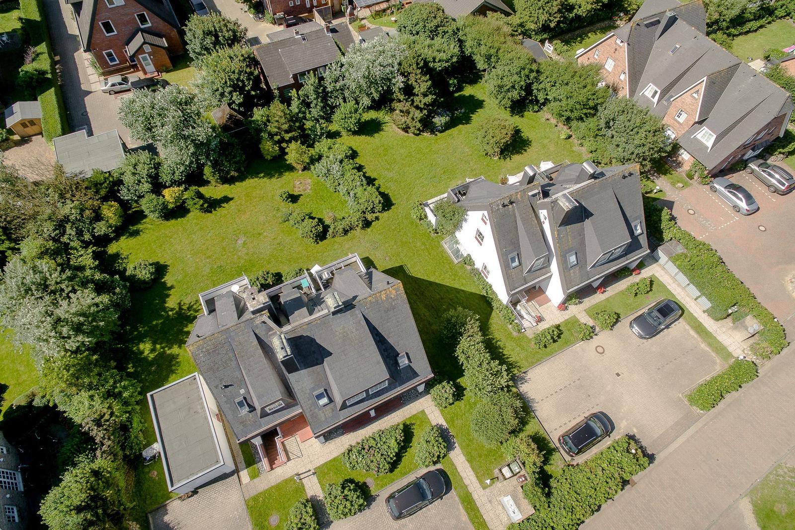 Aerial view of several houses with green lawns and parked cars.