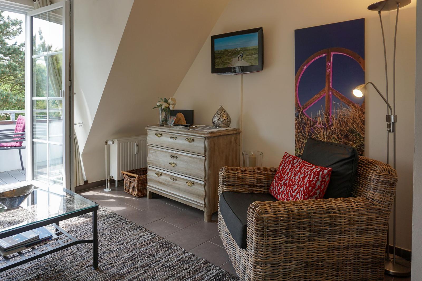 Living room with armchair, dresser, and TV. Window to terrace.