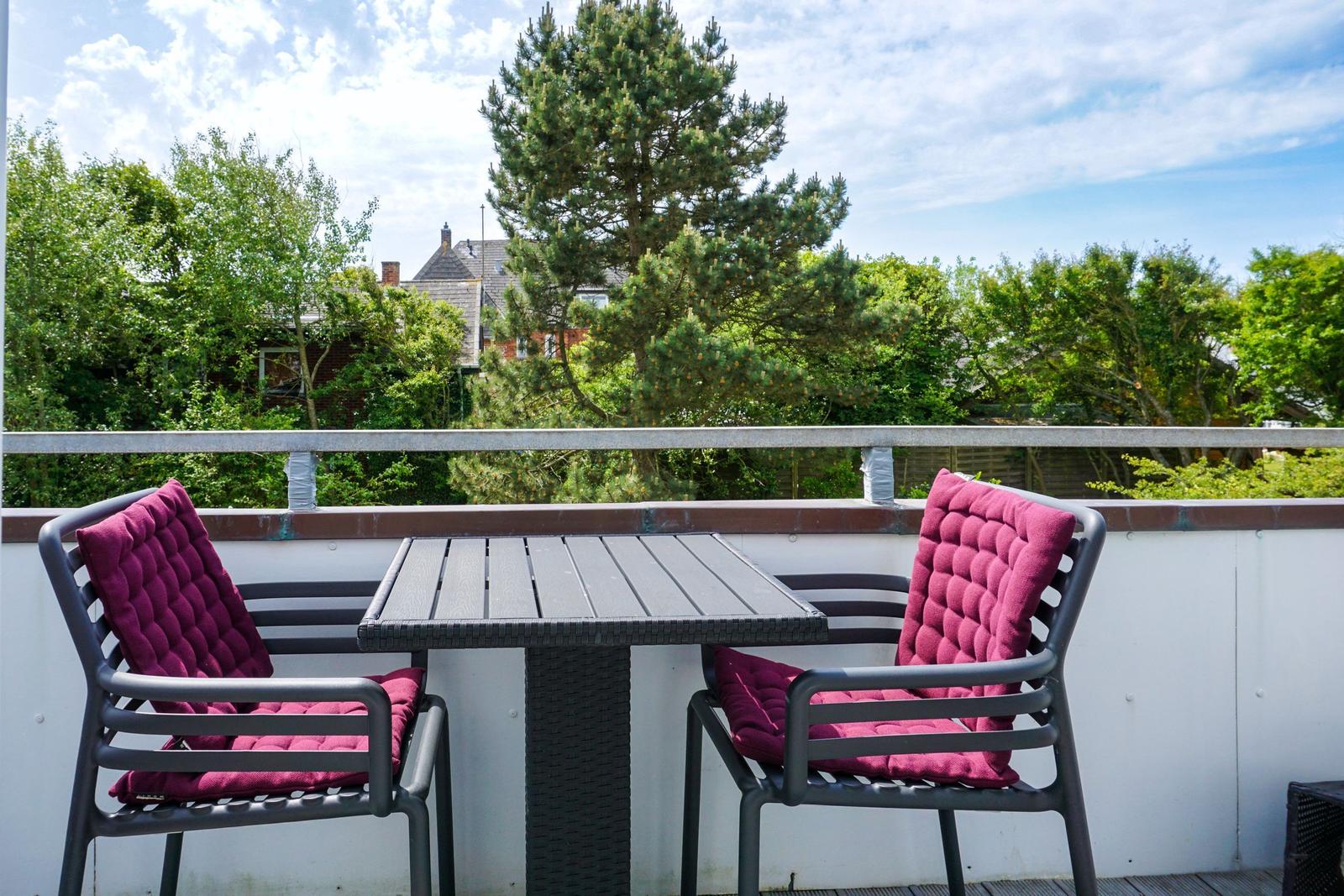 Terrace with table and two chairs with purple cushions. View of trees and sky.