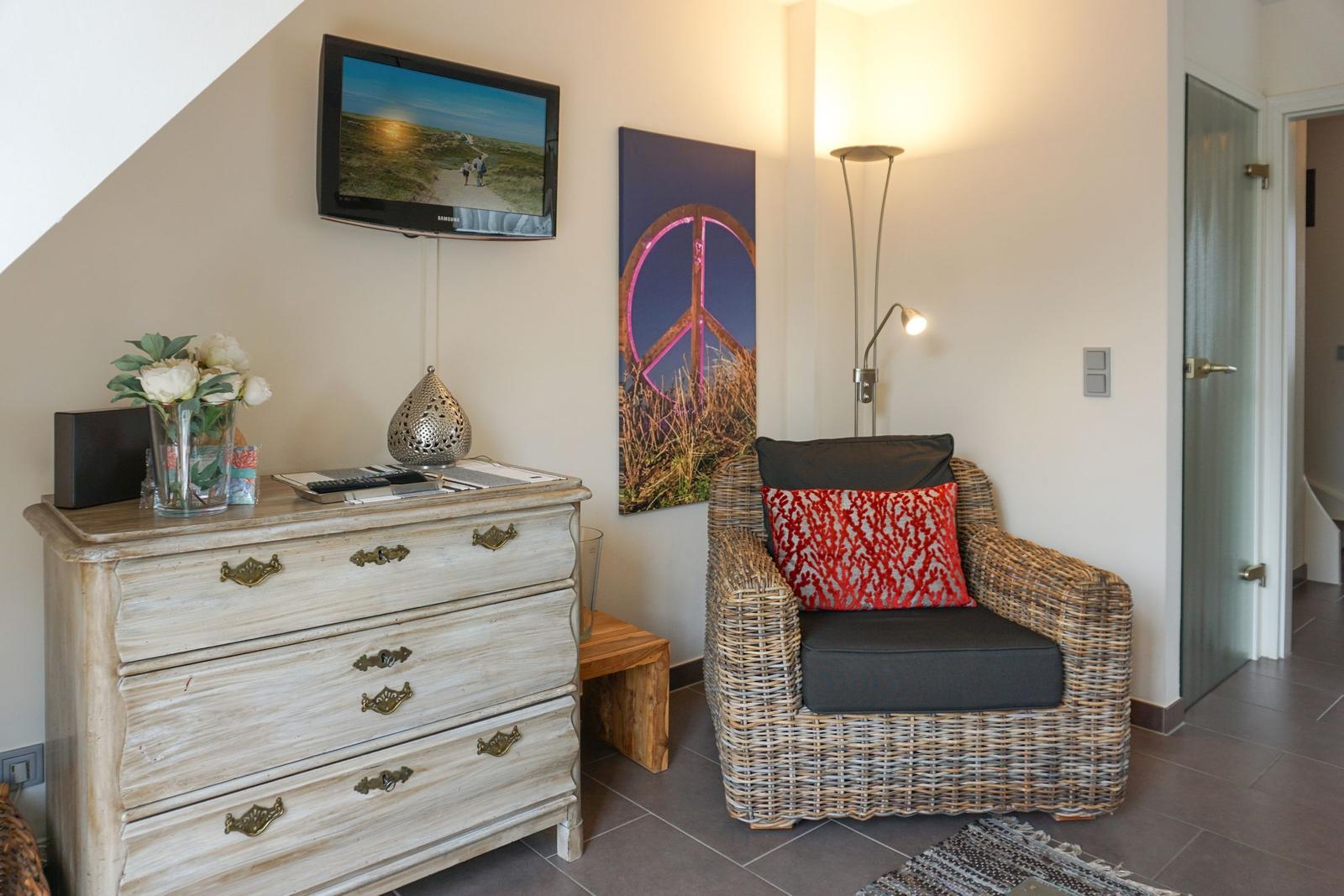 Living room with TV, dresser, and armchair. Wall art and floor lamp visible.