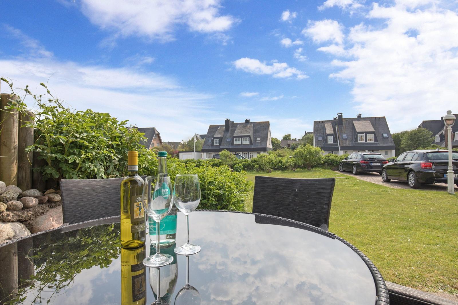 Round table with wine and water glasses in the garden. Houses and cars are visible in the background.