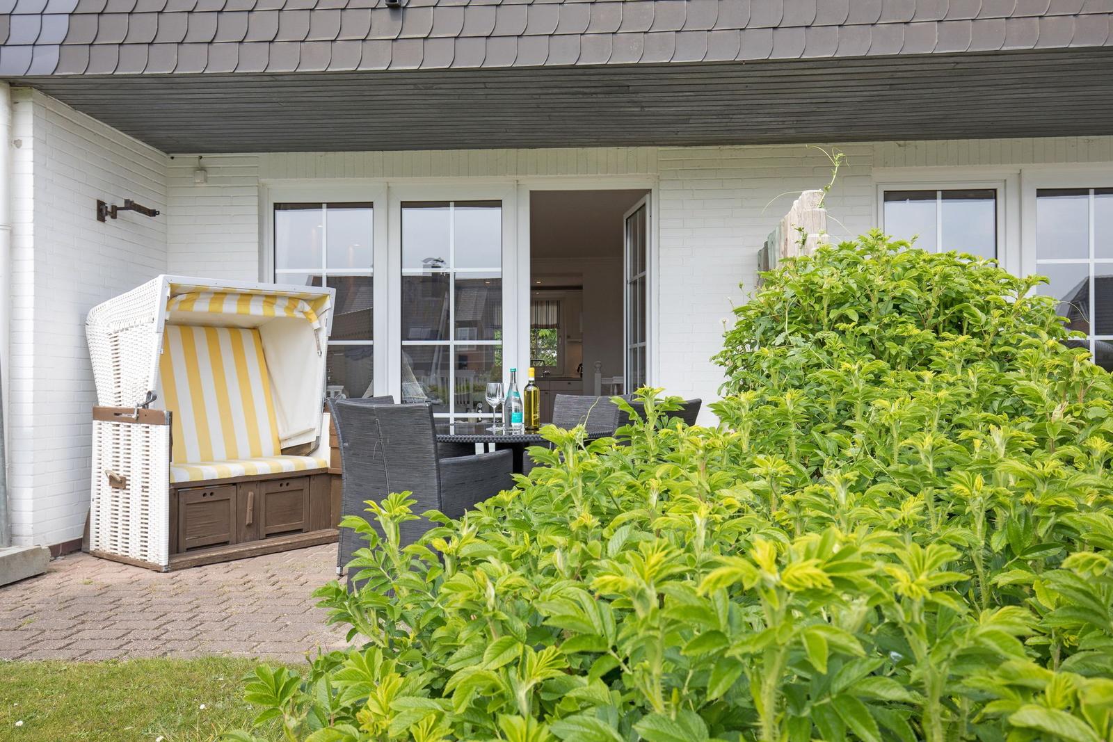 Terrace with beach chair, table and chairs. Backyard with green shrubs.