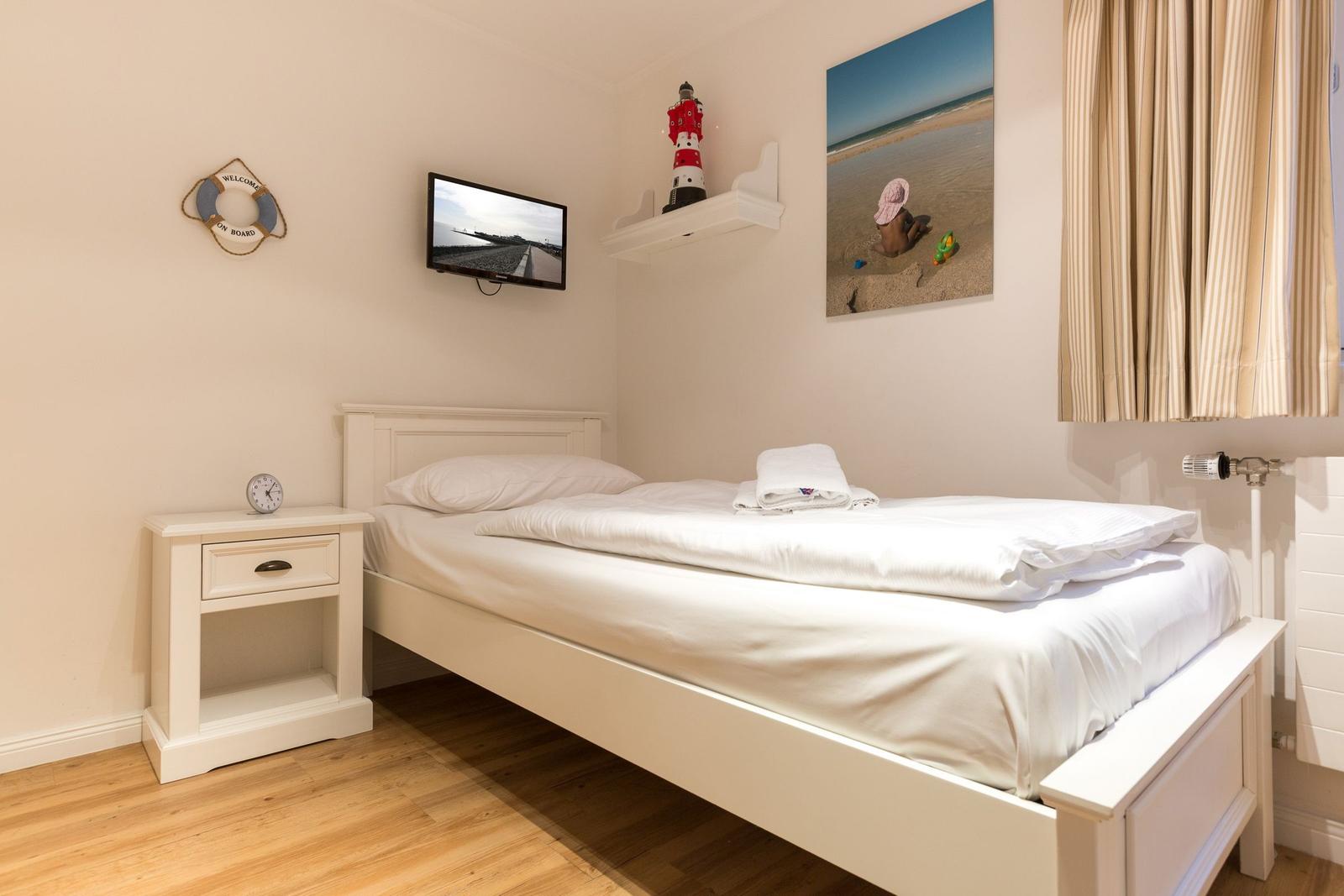 A bedroom with a white bed, nightstand, and wall-mounted TV.