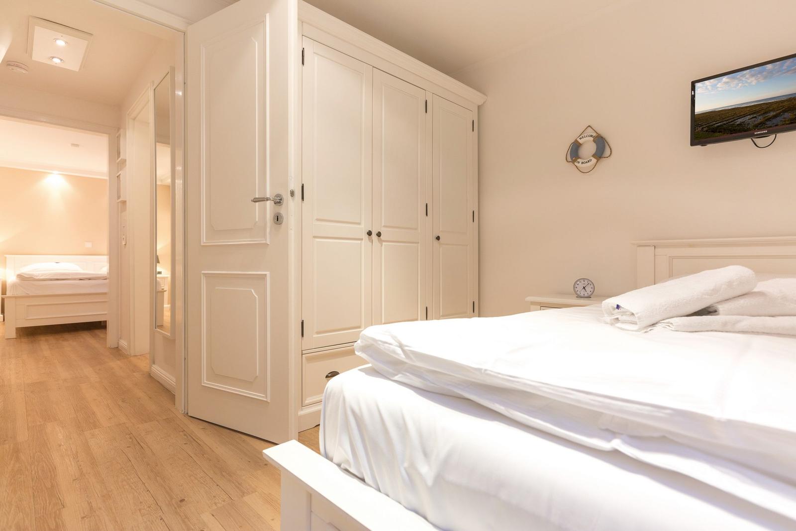 Bedroom with white bed, wardrobe, and TV on the wall.