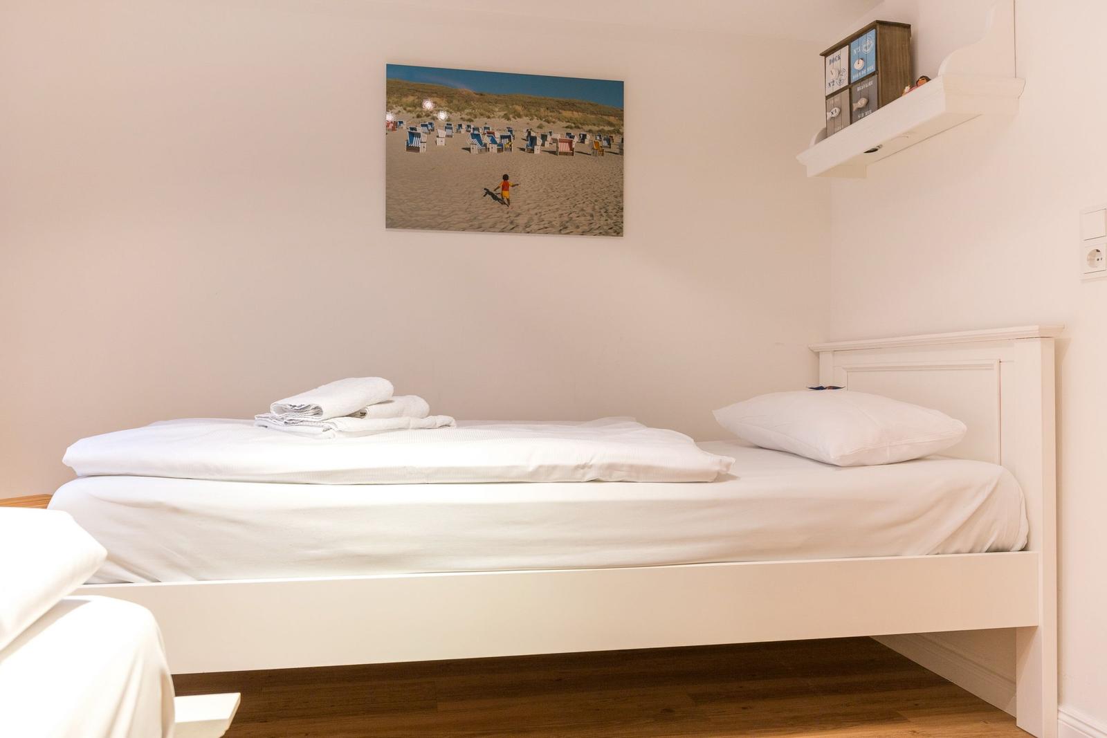 A bed with white bedding, wall picture, and shelf on the wall.