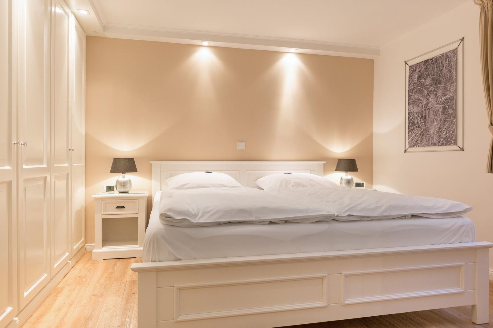 Bedroom with white bed, nightstands, and wardrobe. Wall lighting and picture on the wall.