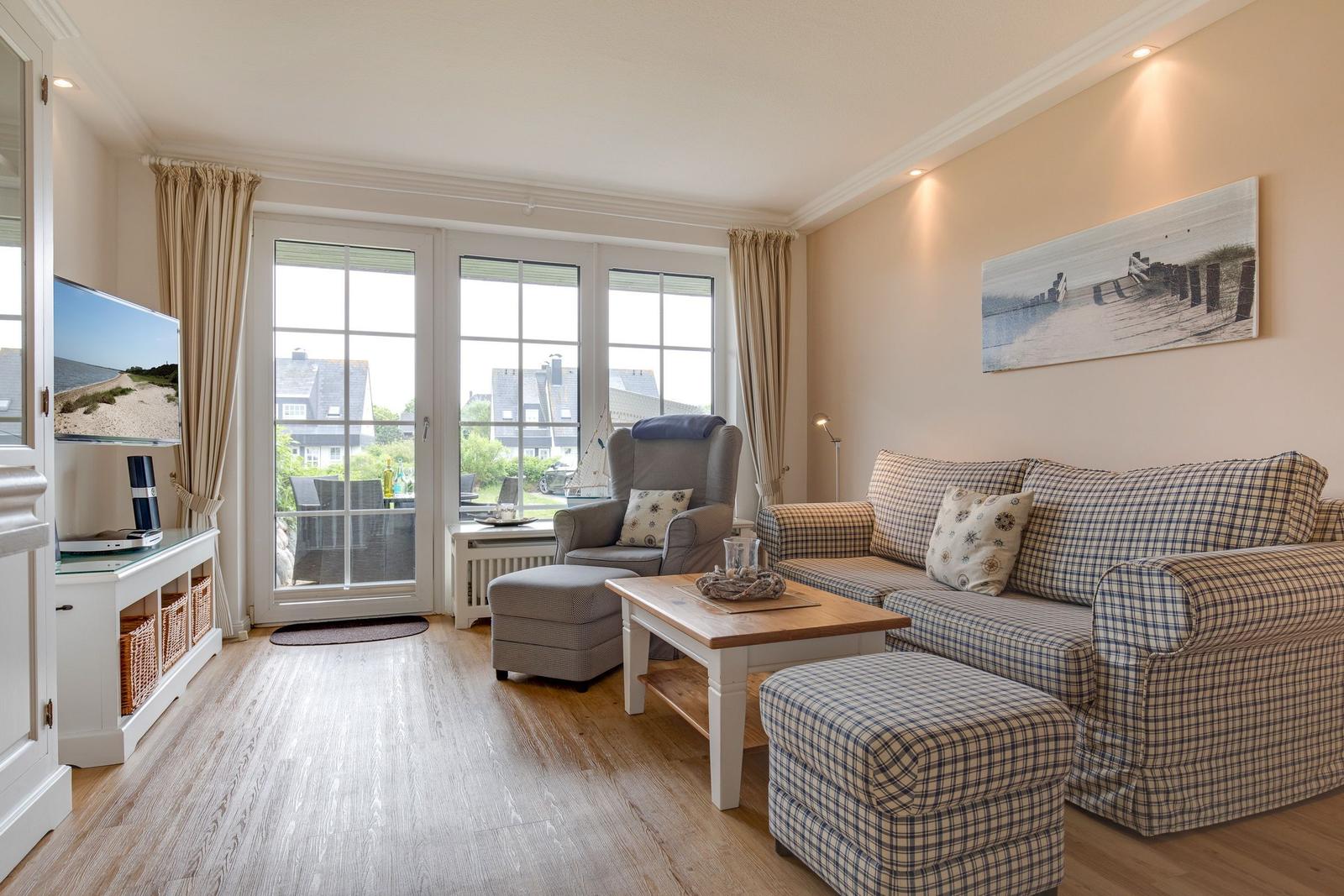 Living room with sofa, armchair, and TV. Large window view to outside.