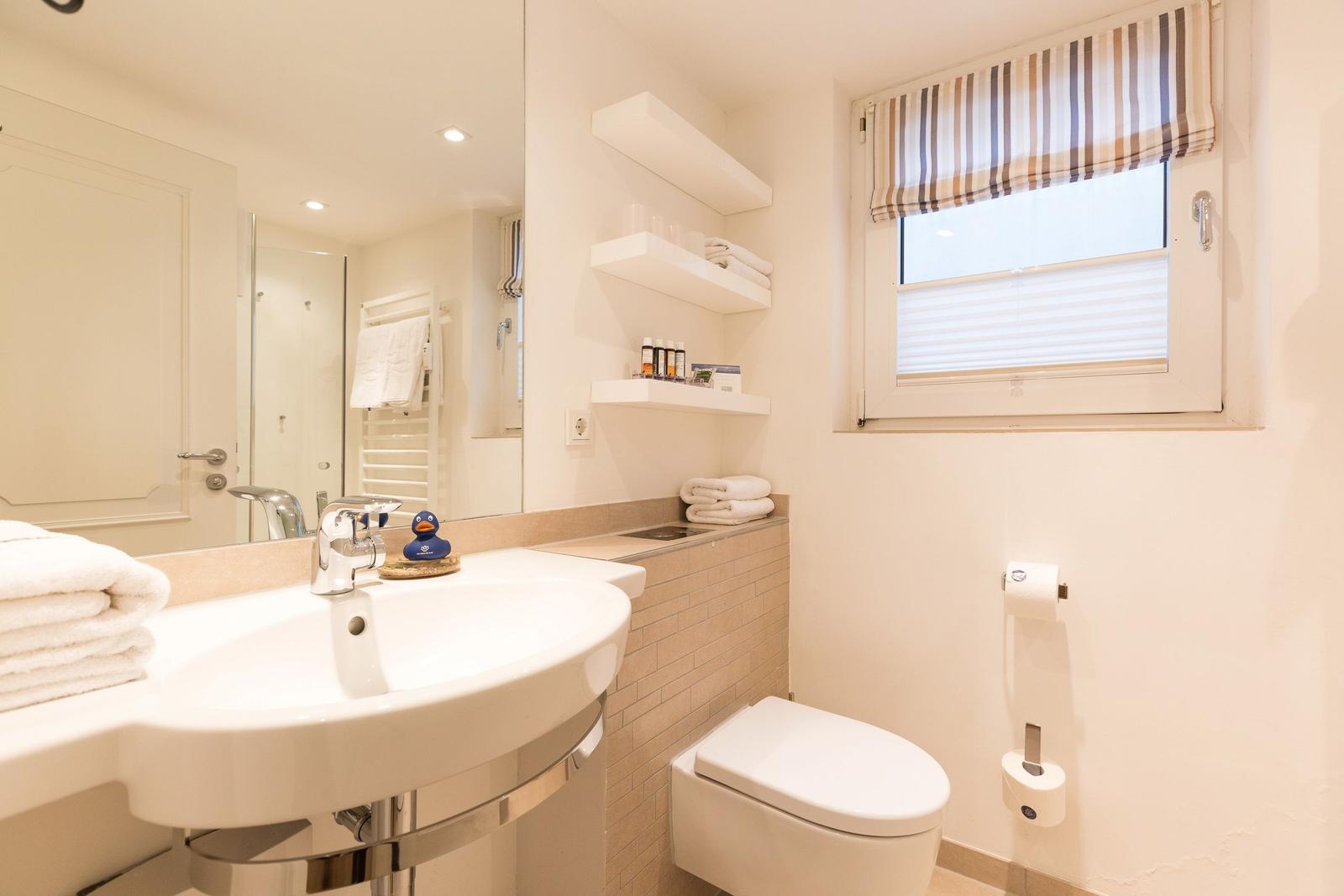 Bathroom with sink, toilet, and window with roller blind.