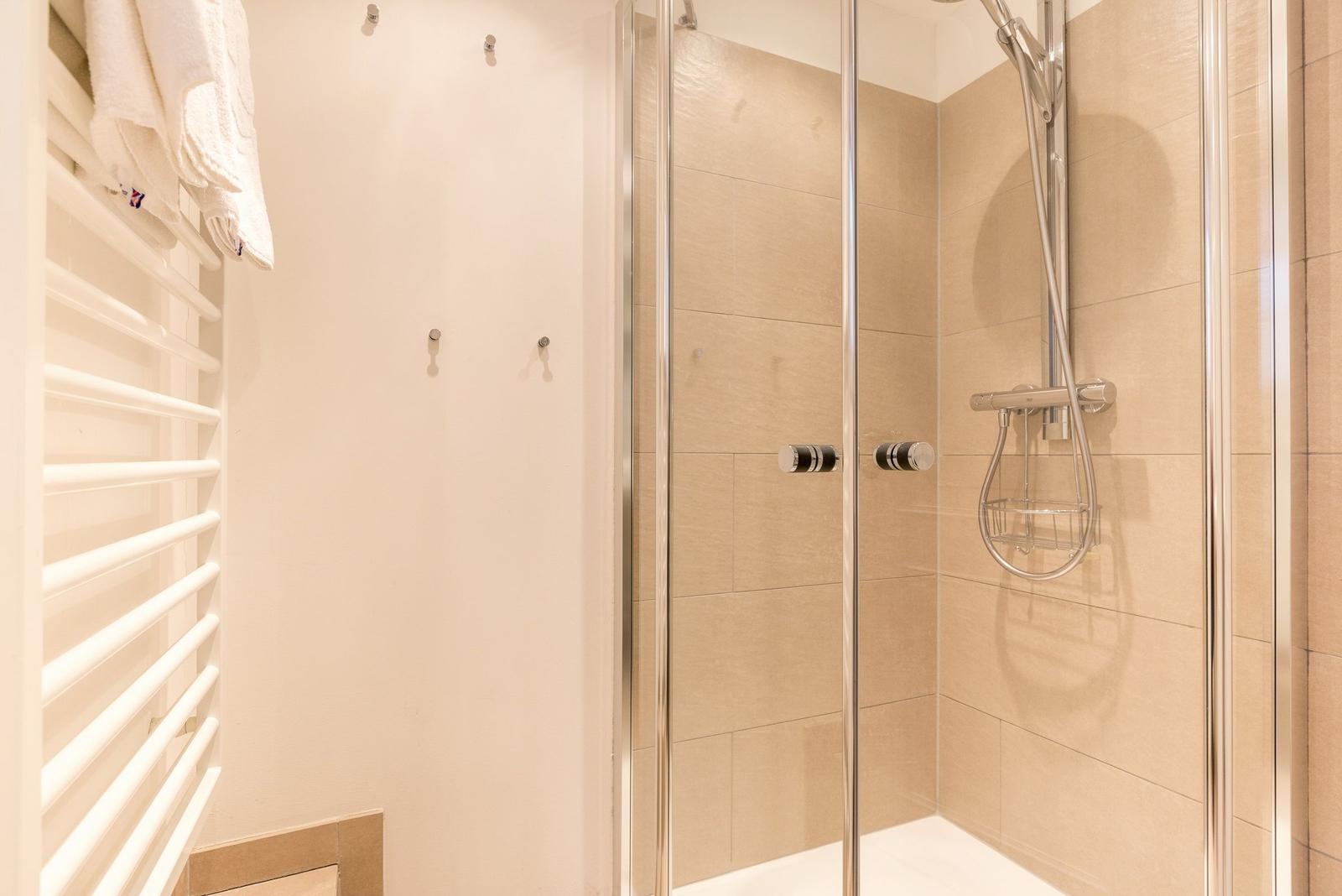 Shower with glass enclosure and handheld shower, next to towel warmer.