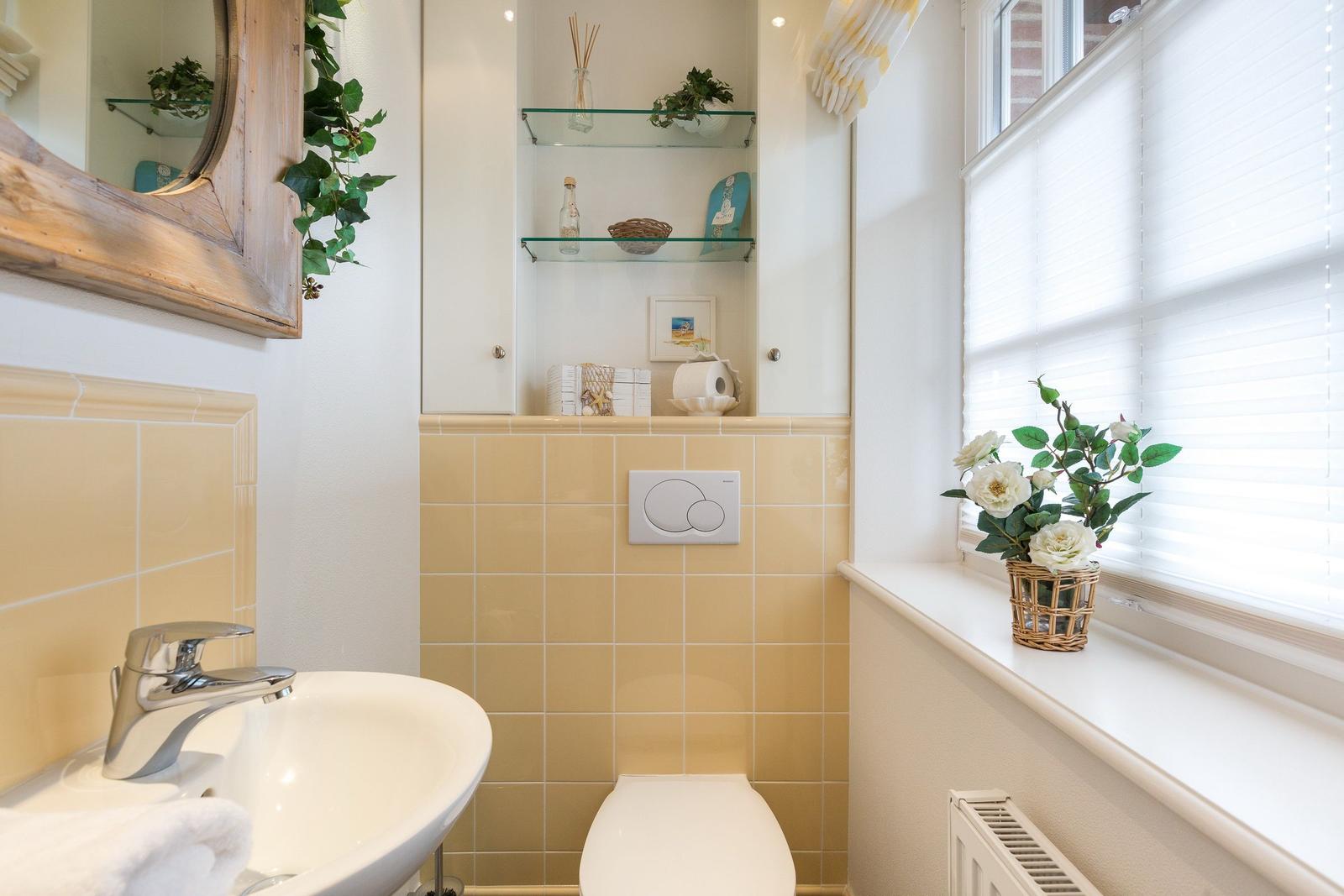 Badezimmer mit Waschbecken, Toilette und Fenster mit Blumen.