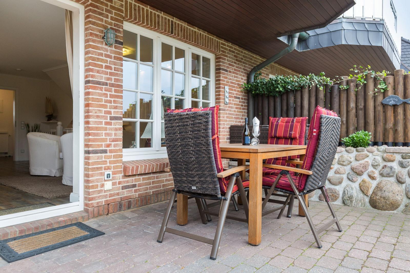 Terrasse mit Holztisch, Stühlen und Sitzgelegenheit. Hinterhof mit Steinmauer und Holzzaun.