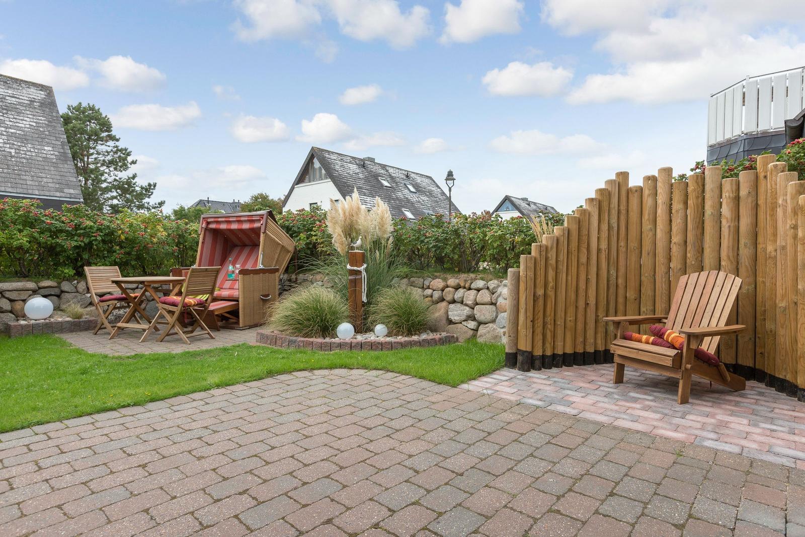 Garten mit Terrasse, Liege, Tisch und Stühle, Holzzaun und Grünflächen.