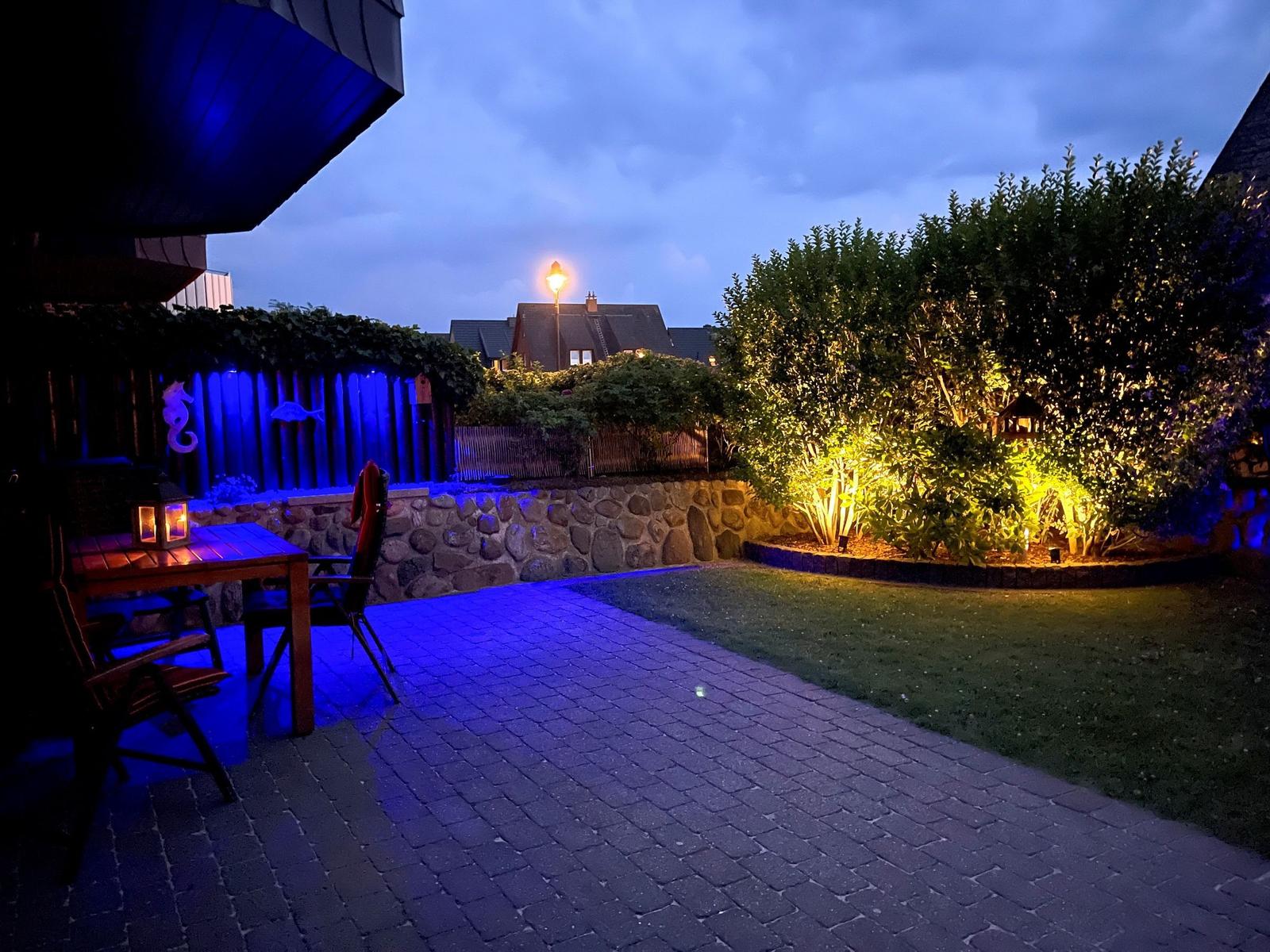Terrasse mit Tisch, Stühlen und Beleuchtung im Garten bei Dämmerung.