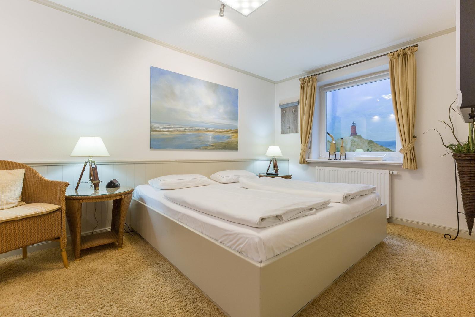 Schlafzimmer mit Doppelbett, Fenster mit Leuchtturmansicht und Wicker-Sofa.