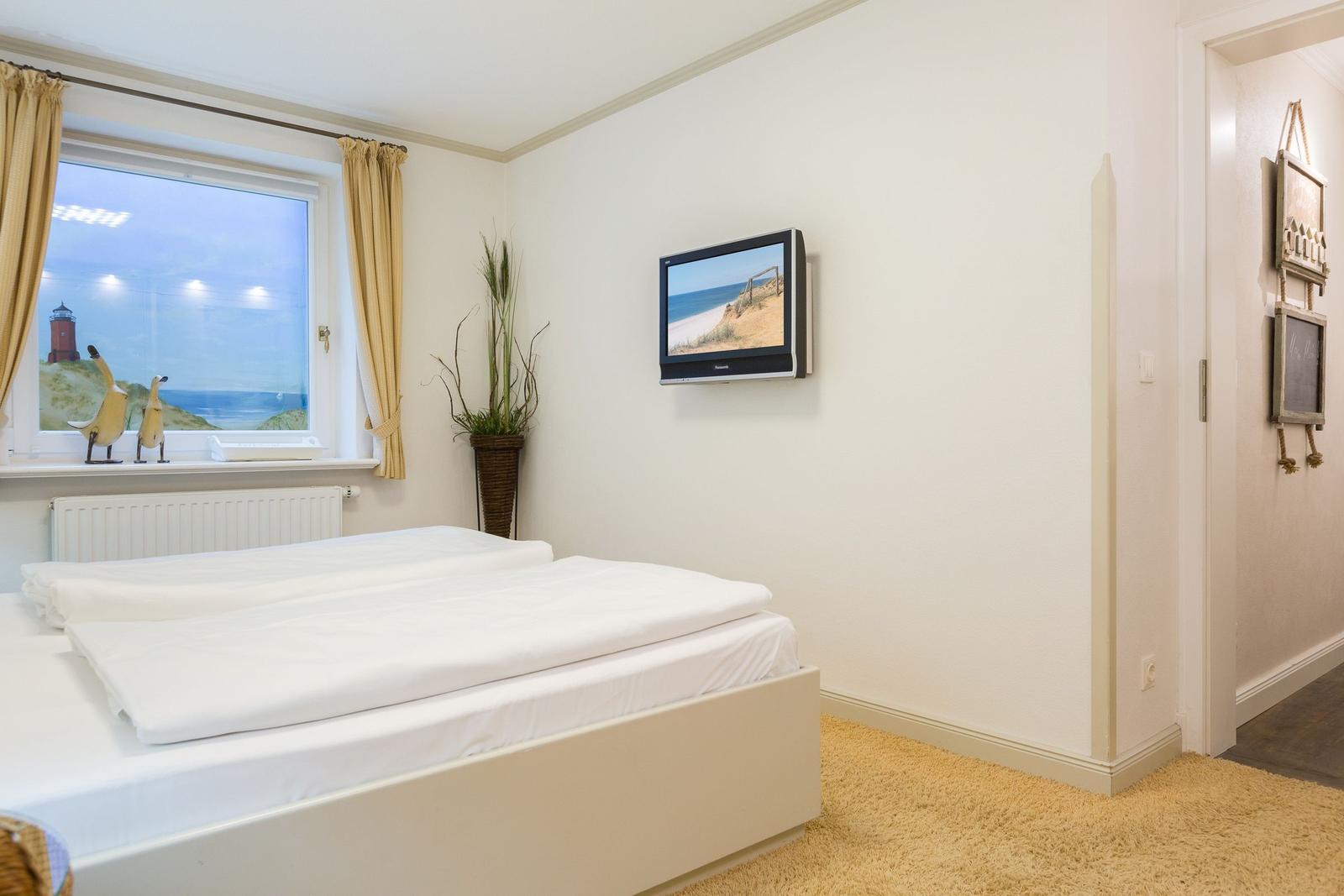 Schlafzimmer mit Bett, TV und Fenster mit Blick auf Leuchtturm.