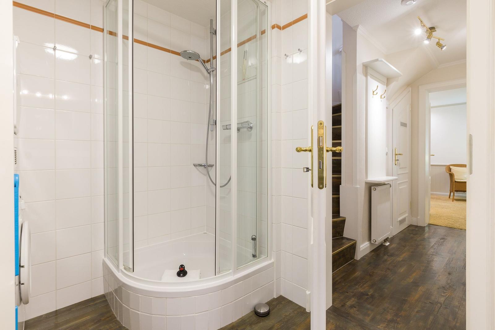 Dusche mit Glaswand und Duschbrause im Bad. Flur mit Treppe und Tür.