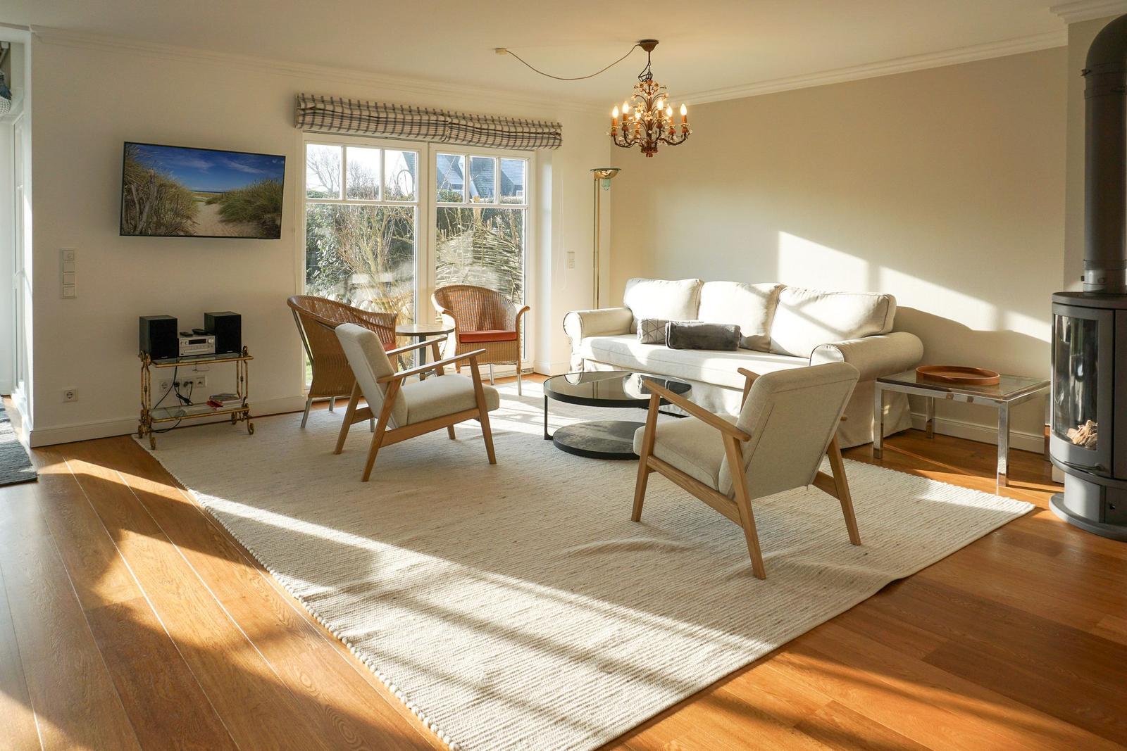 Living room with sofa, chairs, and fireplace. Windows, TV, and chandelier visible.