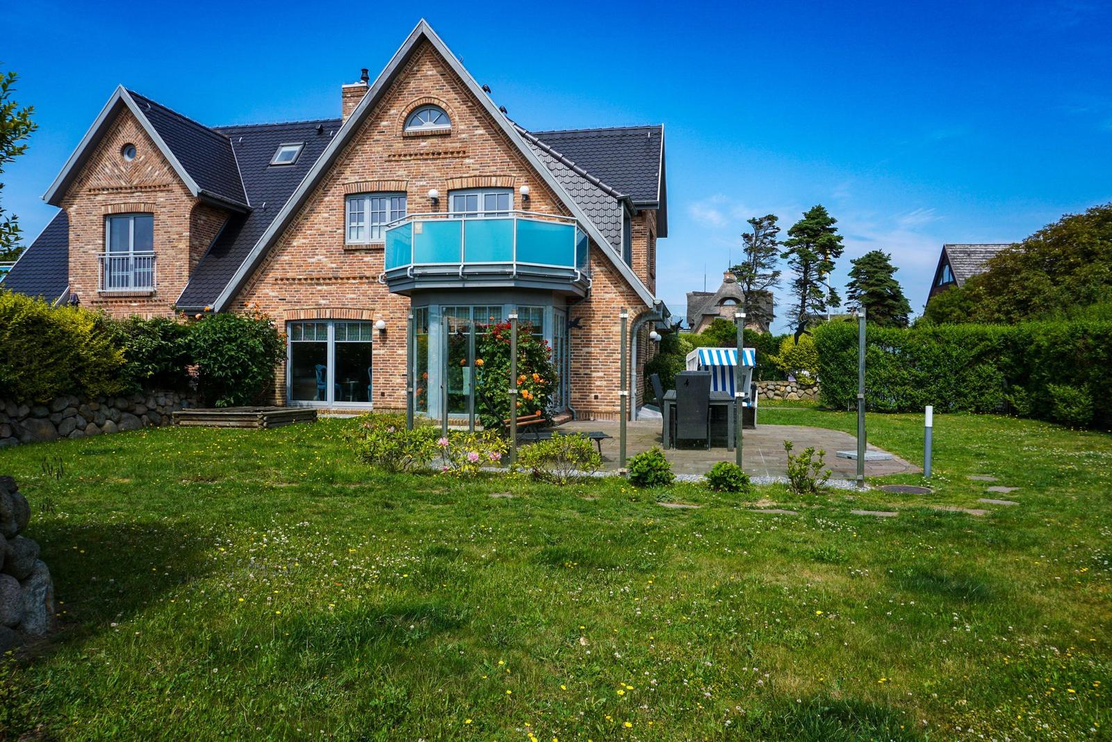 A two-story house with balcony and garden. Blue sky and green grass.