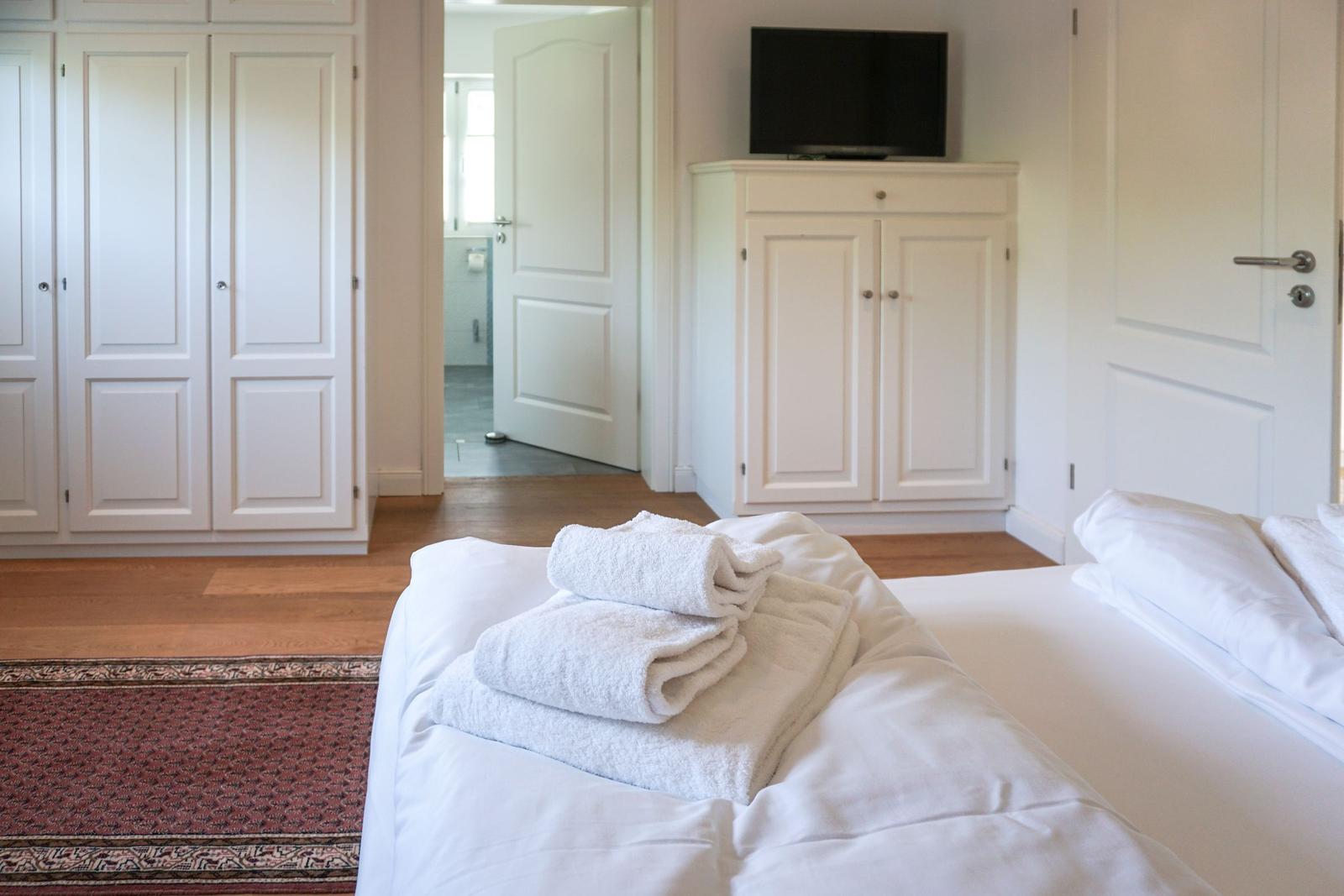 Bedroom with bed, towels, wardrobe, and TV.