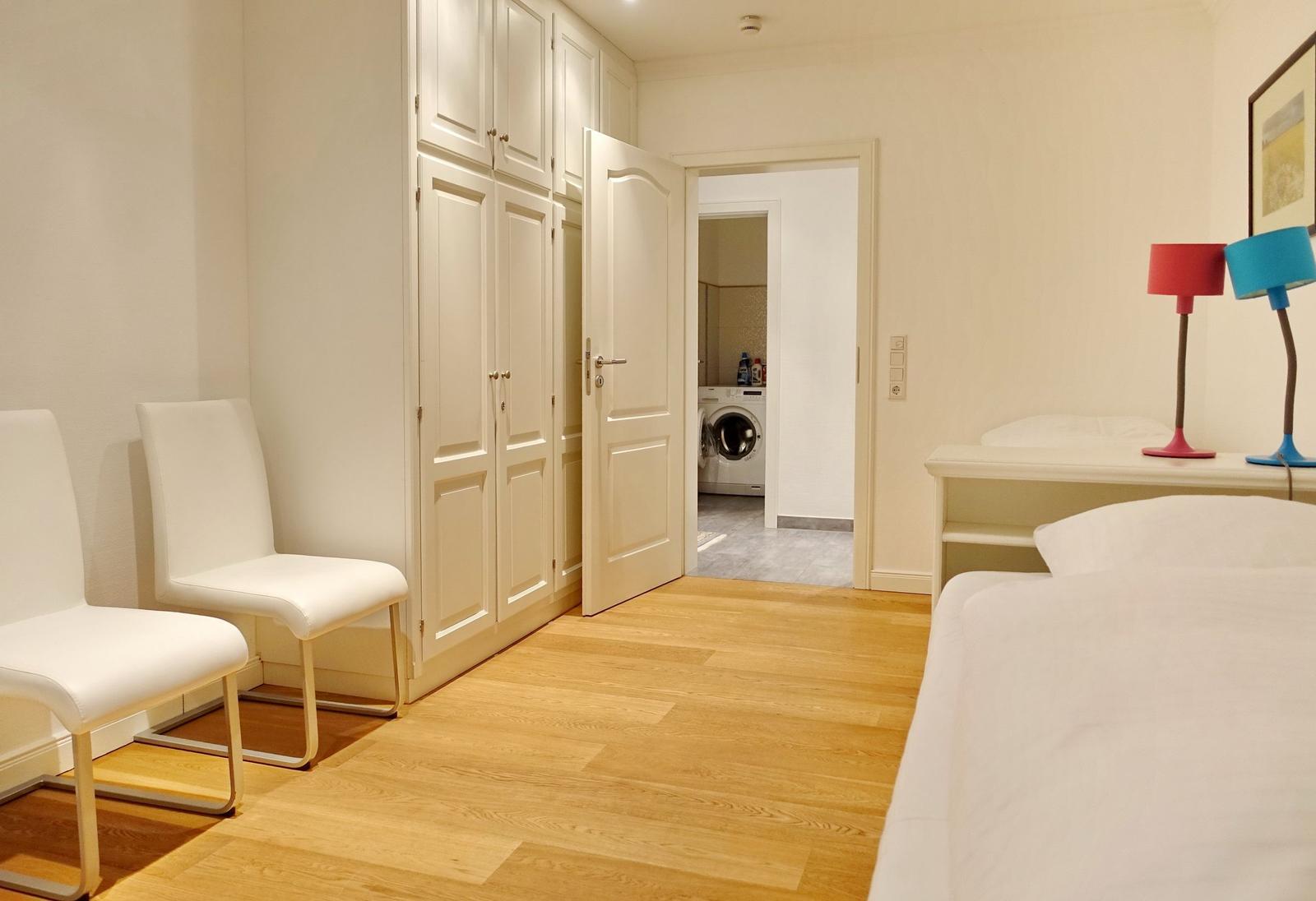 Bedroom with bed, desk, chairs, and wardrobe. Hallway to laundry room.