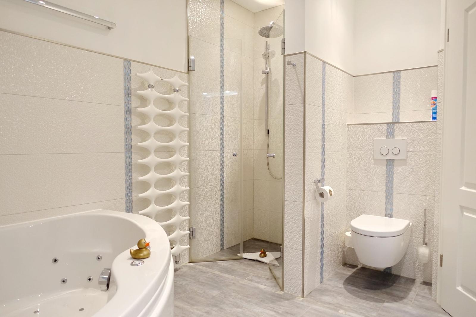 Bathroom with whirlpool, shower, and toilet. White tiles and gray floor tiles.