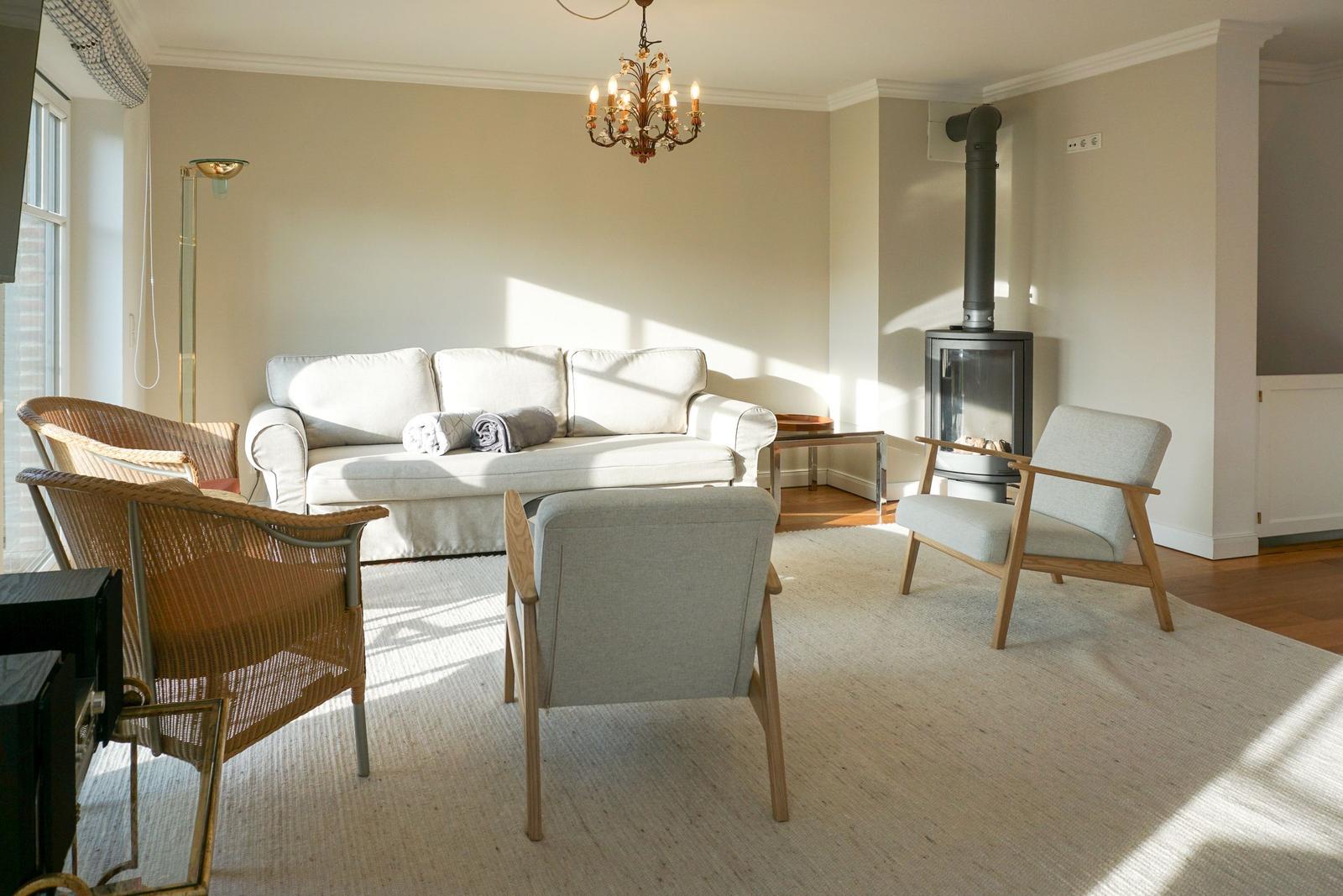 Living room with sofa, armchairs, and wood-burning stove. Hardwood and carpeted floor.