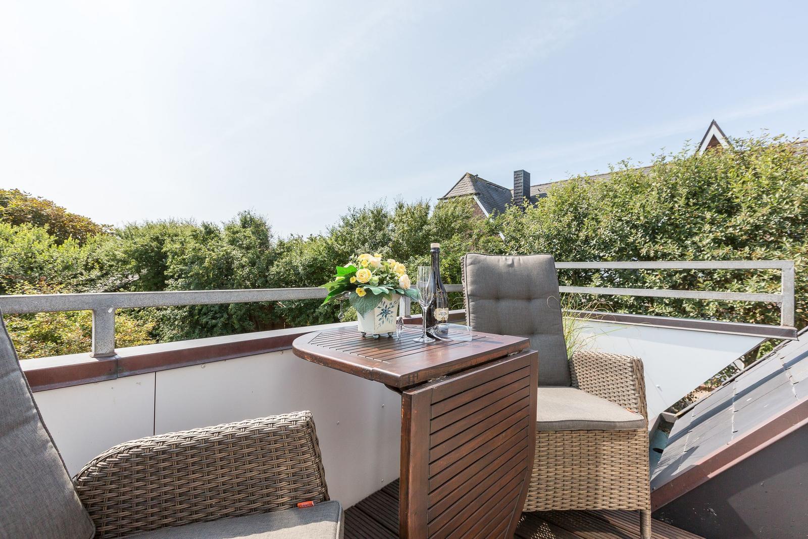 Terrace with table, chairs, and flower arrangement. View of green hedge and roof.