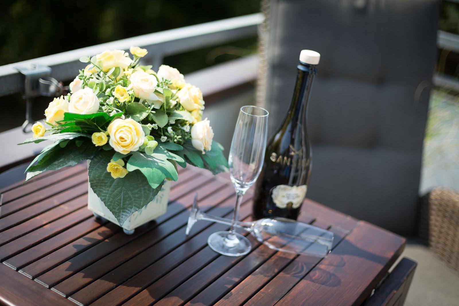 On the terrace, a table holds flowers, a champagne glass, and a bottle.