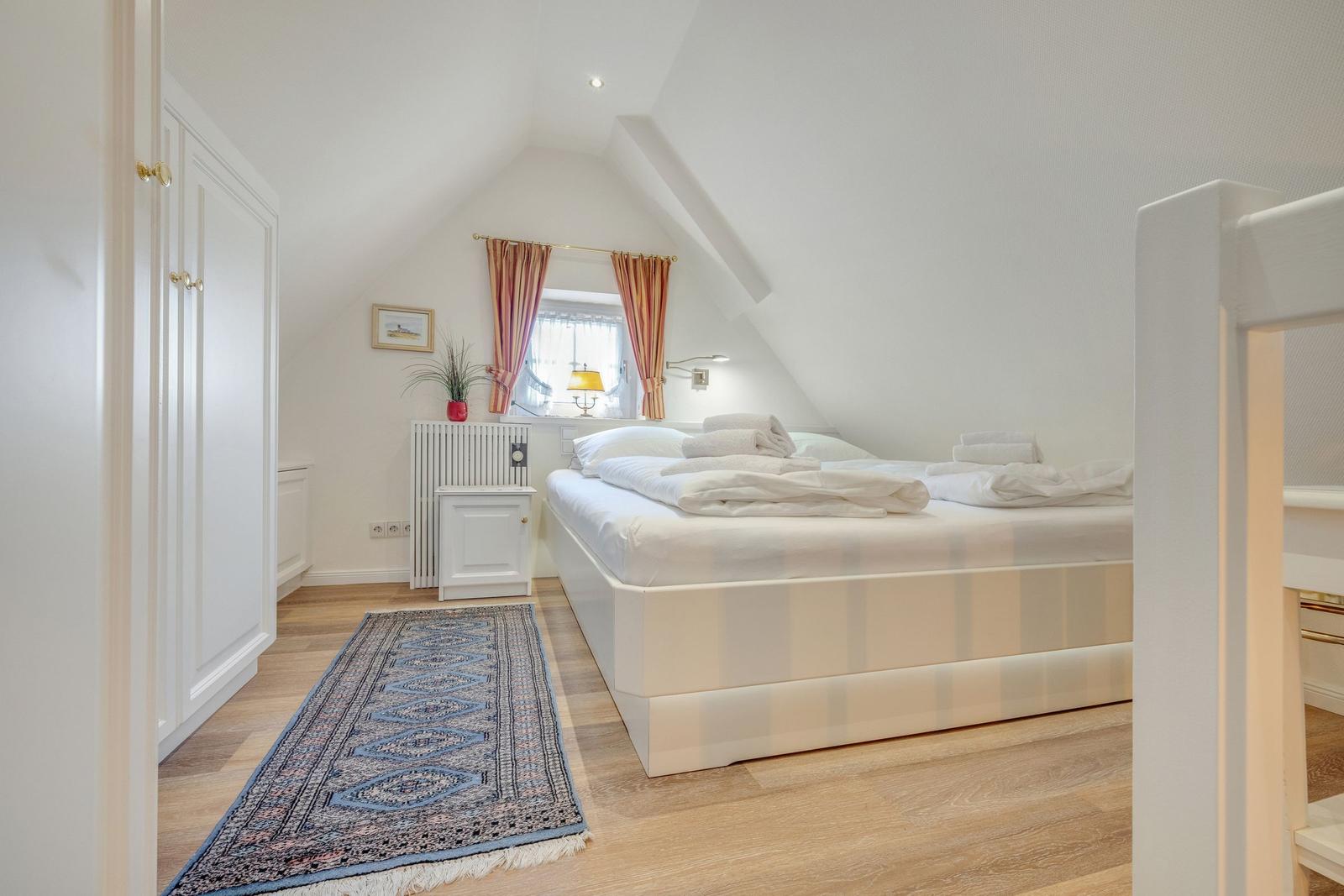 Bedroom with double bed, wooden floor, and window with curtains.