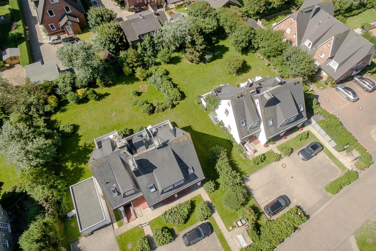 Aerial view of several houses with green gardens and parked cars.