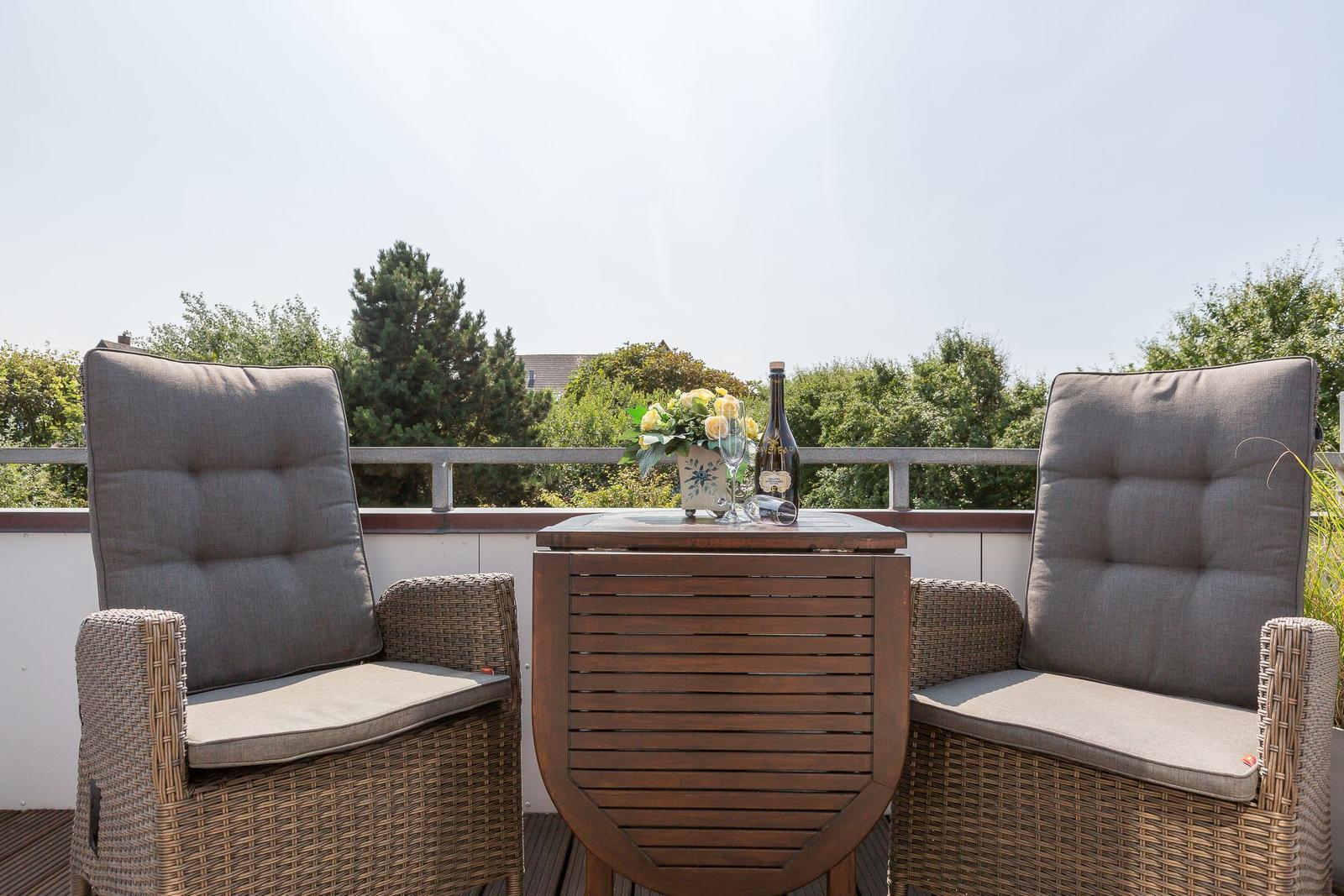 Terrace with two seating areas and table with flowers and bottle.