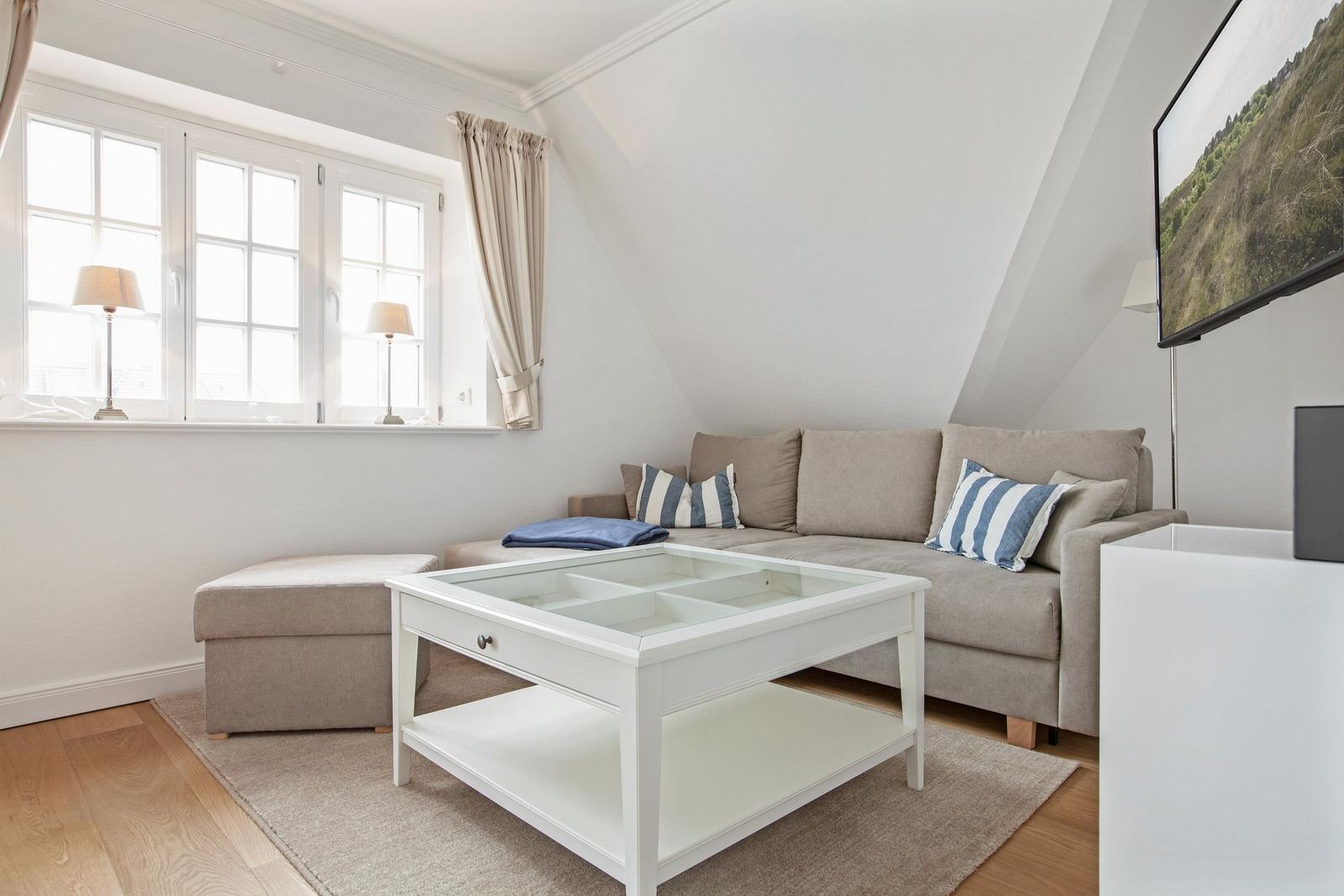 Living room with sofa, glass table, and windows. Attic with wooden floor and wall art.