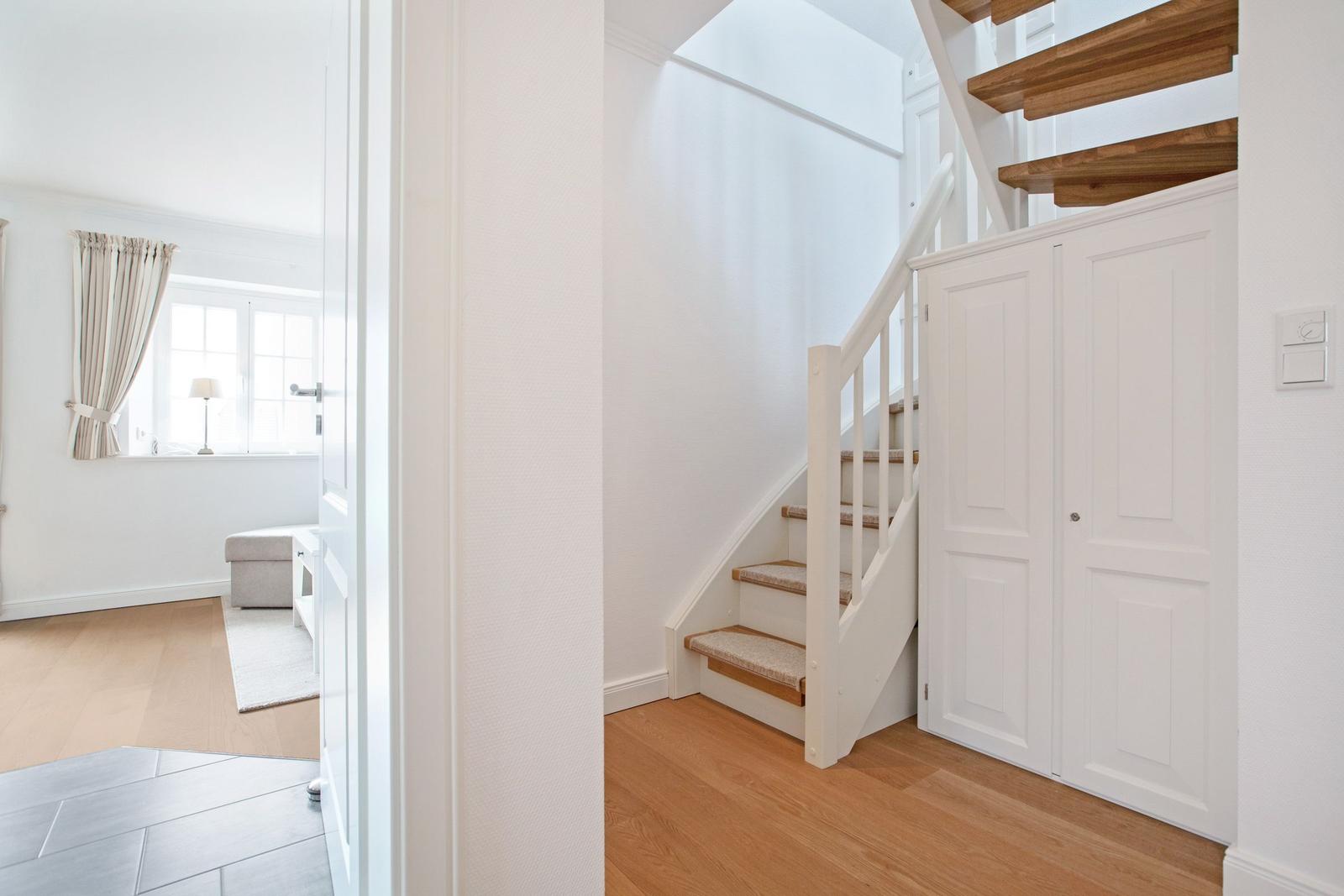 House with staircase and door, view into living room with window and seat.
