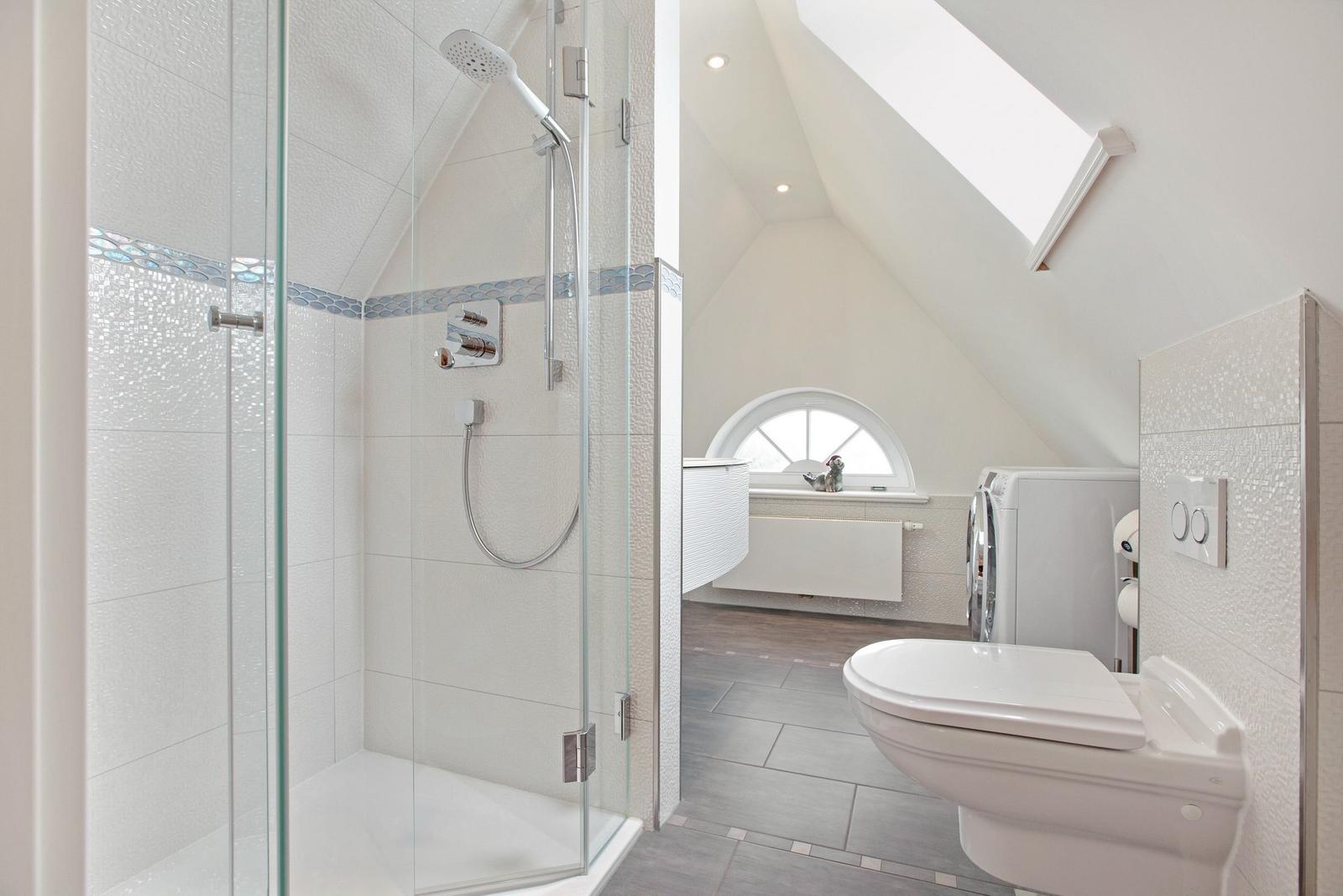 Shower with glass enclosure, toilet, and washing machine under sloped ceilings.
