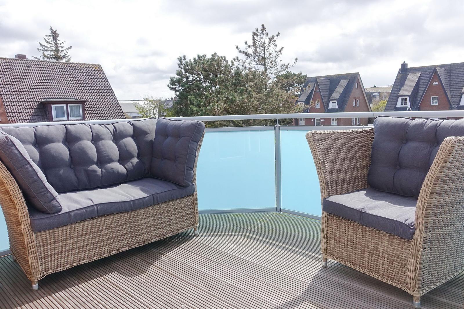 Terrace with rattan sofa and chairs, view of rooftops and trees.