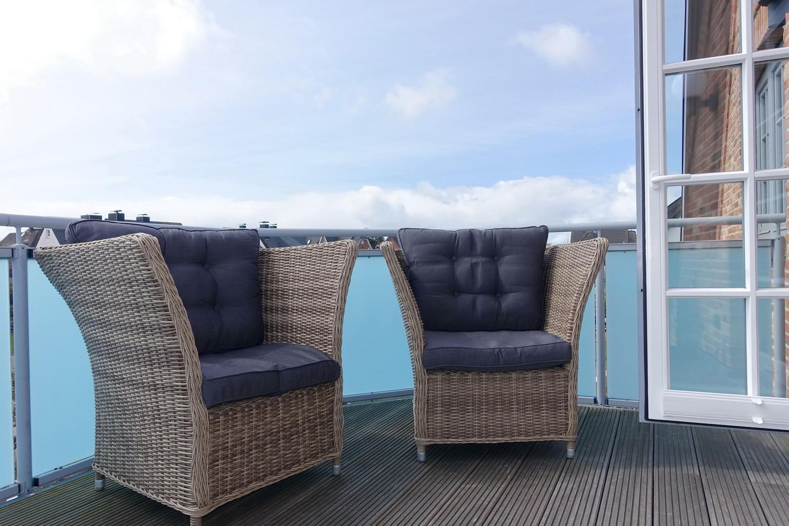 Two chairs with cushions are on the terrace. Background: blue sky and buildings.