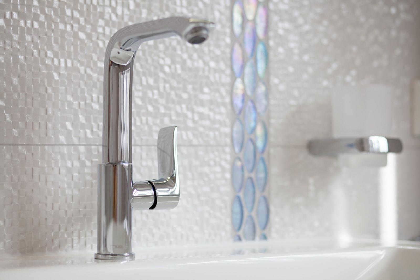 Modern sink with chrome faucet and mosaic tiles in the background.